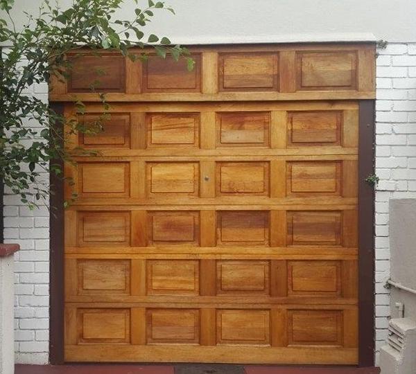Wooden garage door with square panels in a brick-walled setting.
