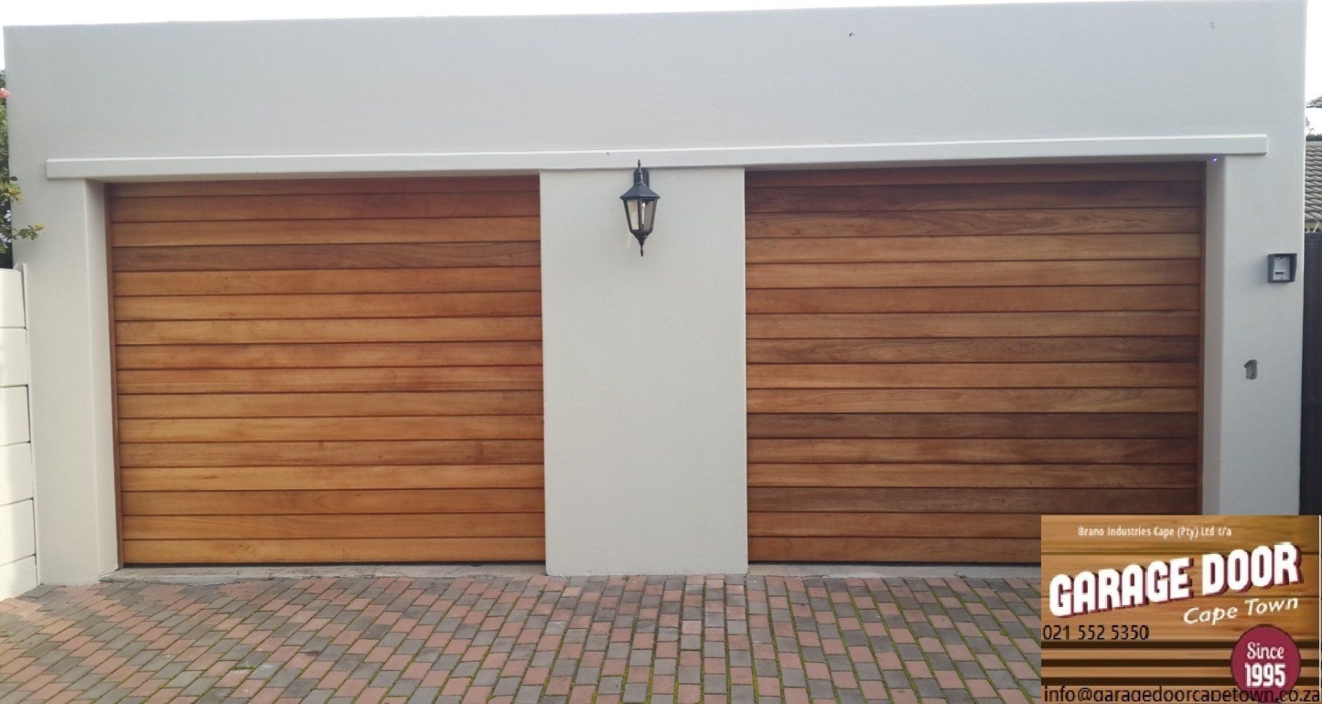 Two wooden garage doors with light brown horizontal panels on a white building.