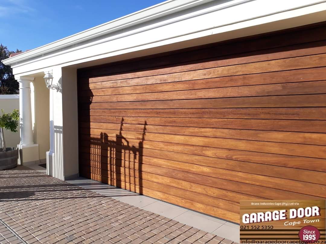 Wooden garage door with a brown finish, with light-colored trim on a house's exterior.