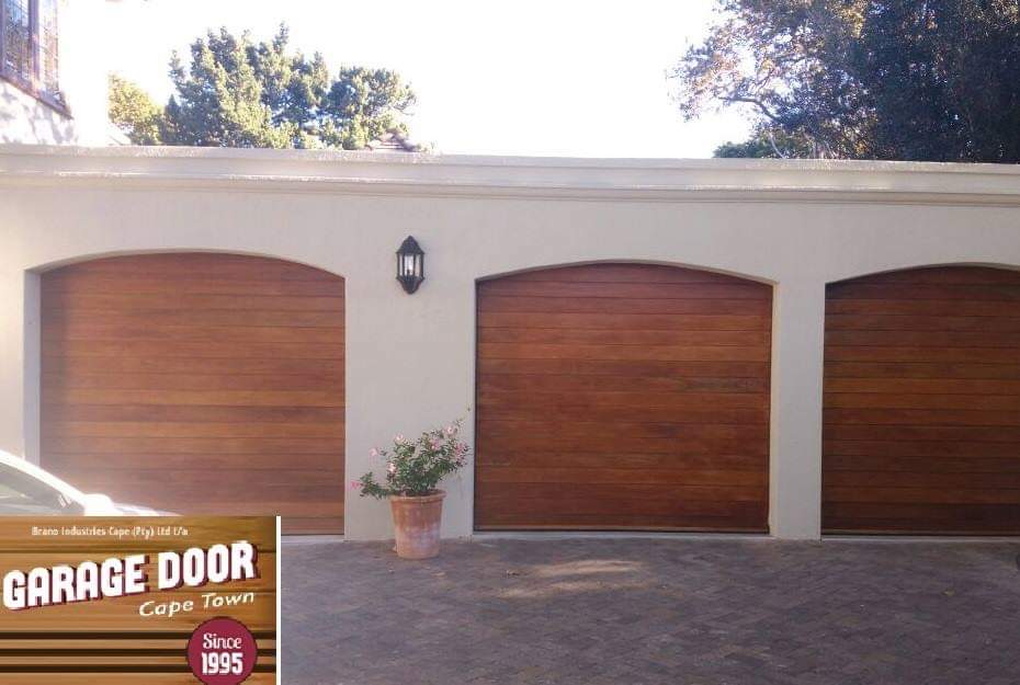 Three wooden garage doors with arched tops, centered on a white building. A car is partially visible on the left.