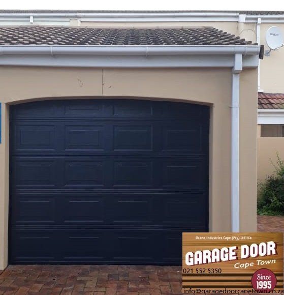 Dark blue garage door in a tan-colored frame with a white gutter.