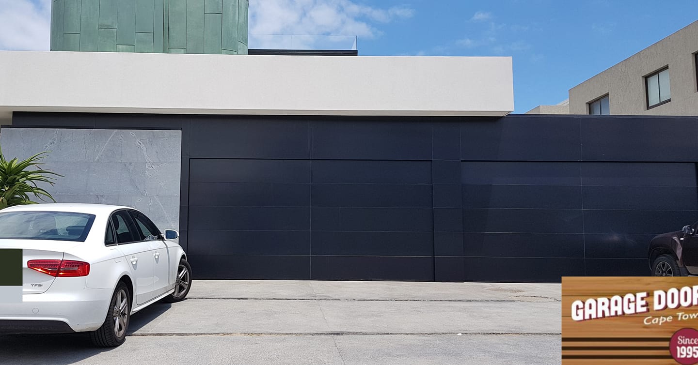 White car parked in front of a modern grey garage with blue sky in the background.