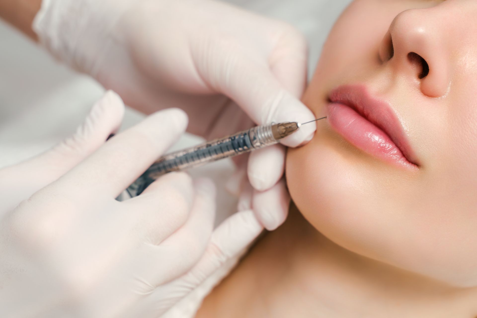 A person receives lip injections; a gloved hand injects the lip with a syringe.