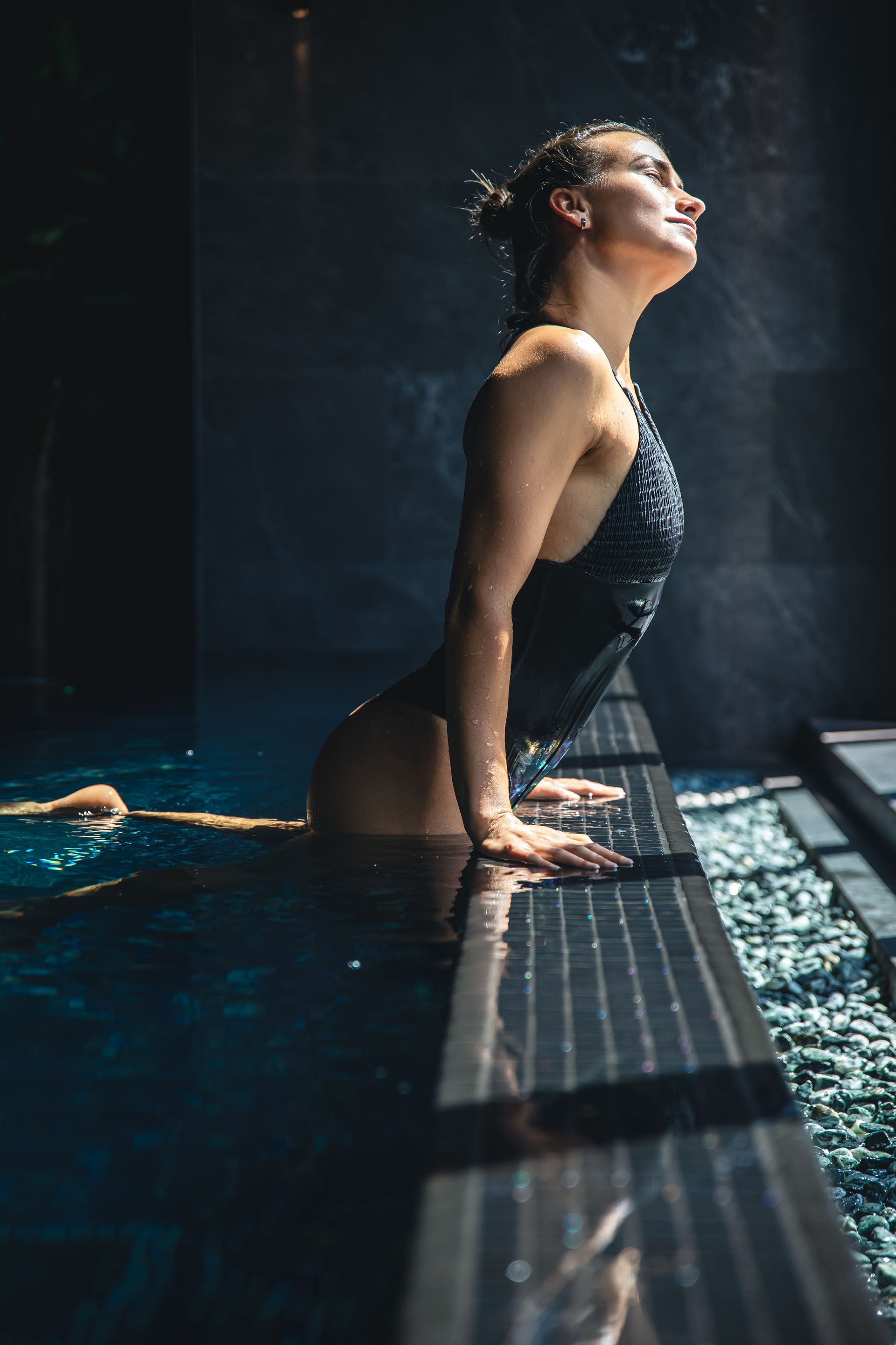 a woman in a black swimsuit is leaning on the edge of a pool