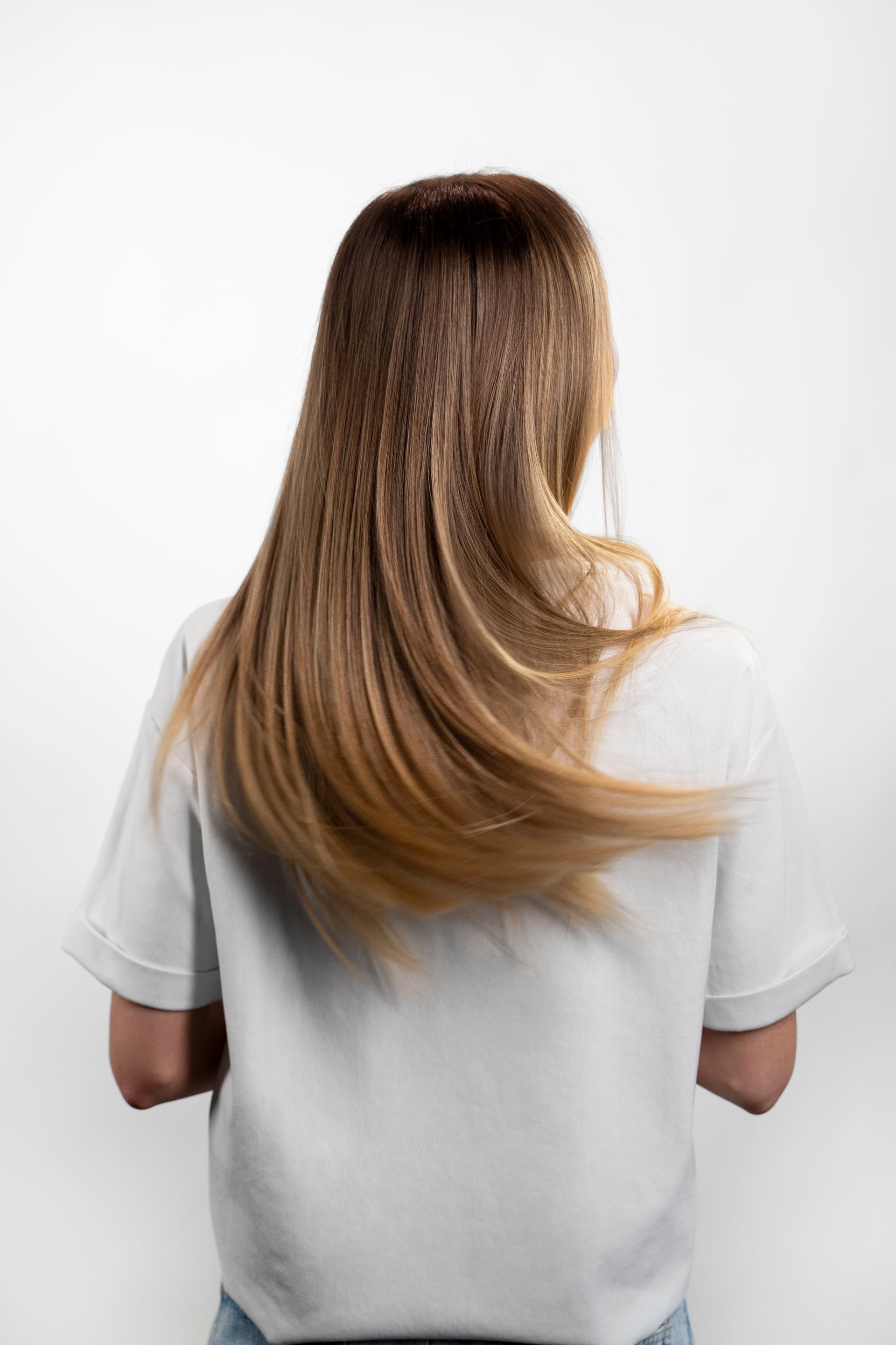 the back of a woman with long hair wearing a white shirt .