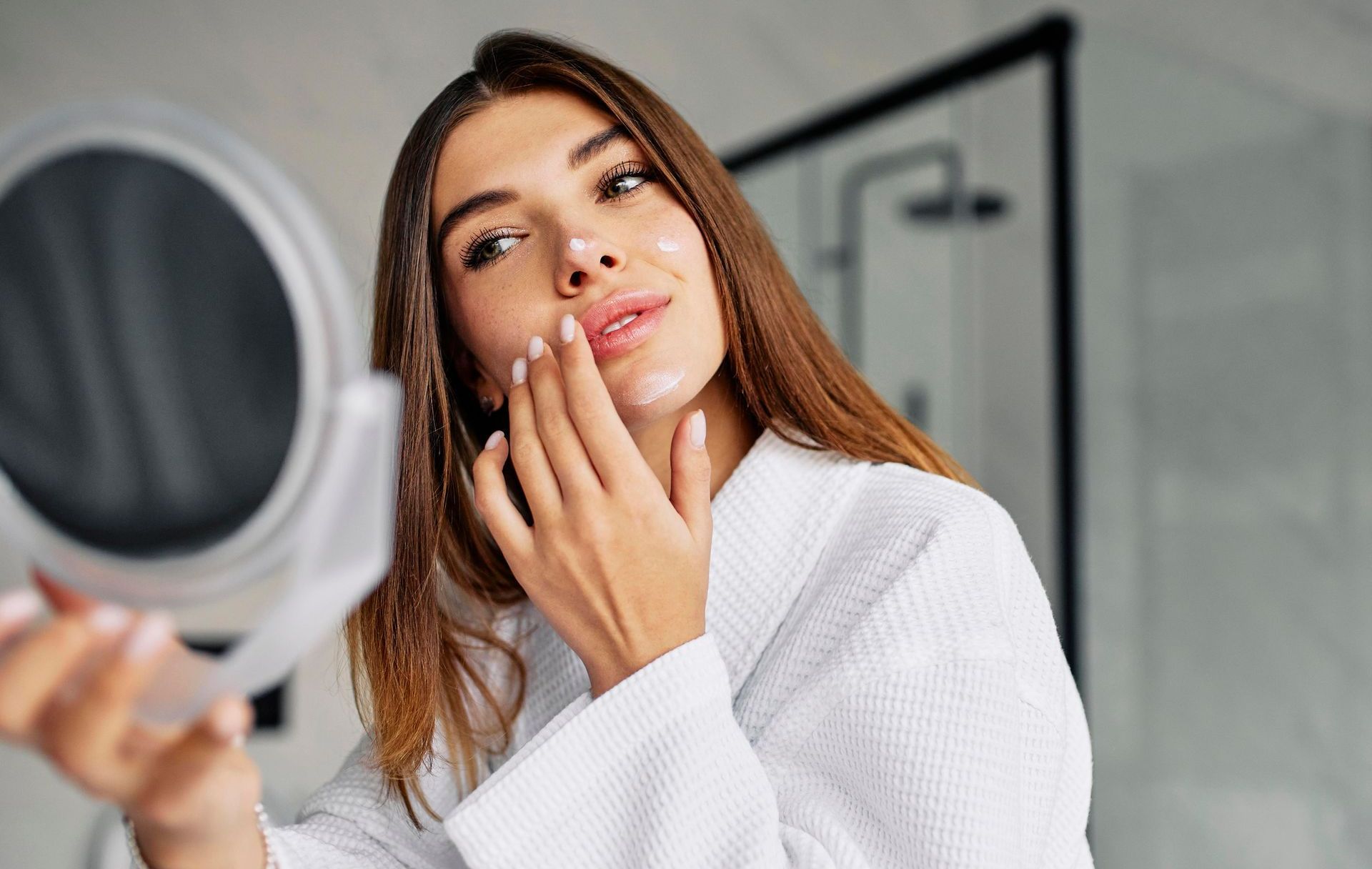 A woman is looking at her face in a mirror.