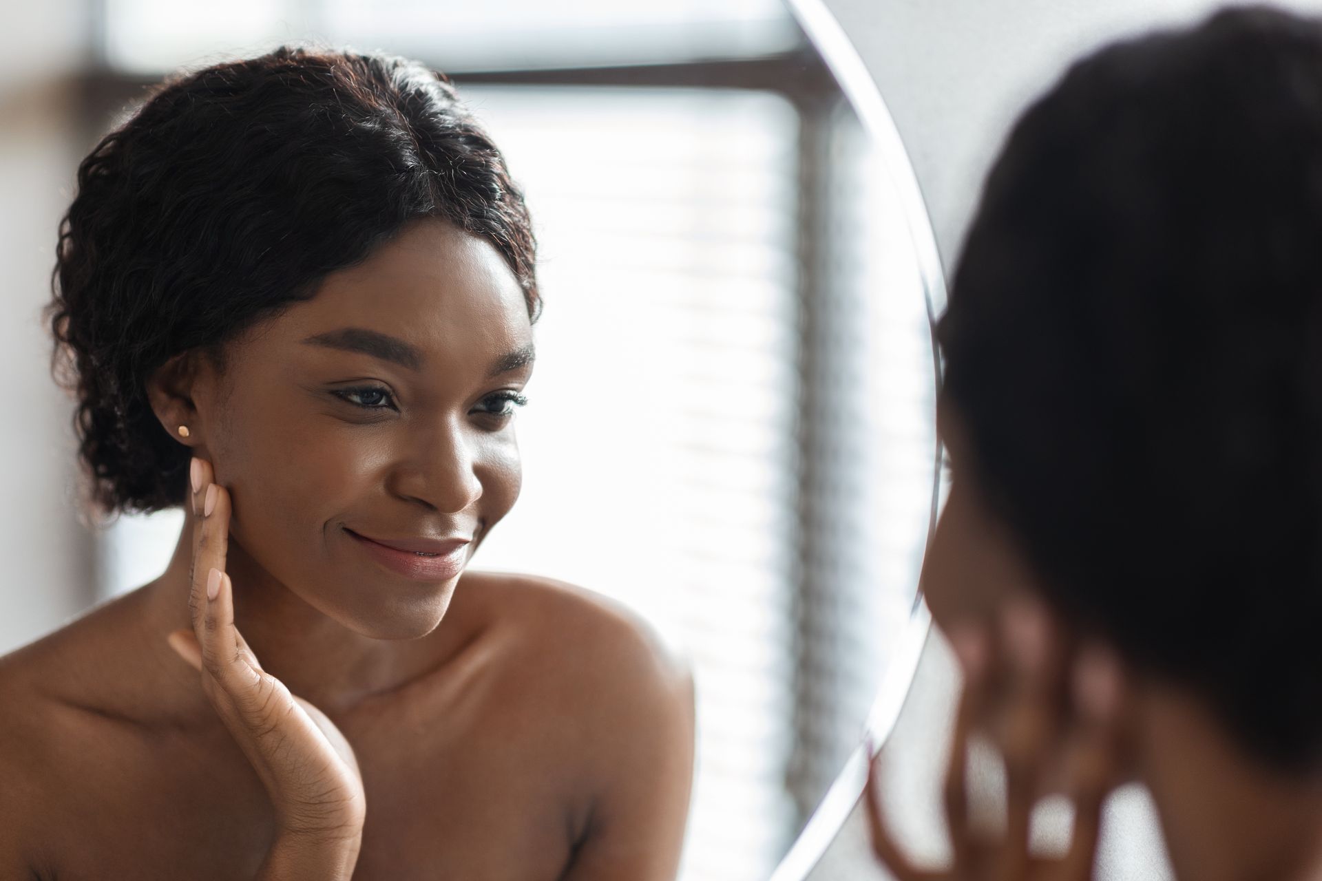 pretty black woman looking at skin in mirror