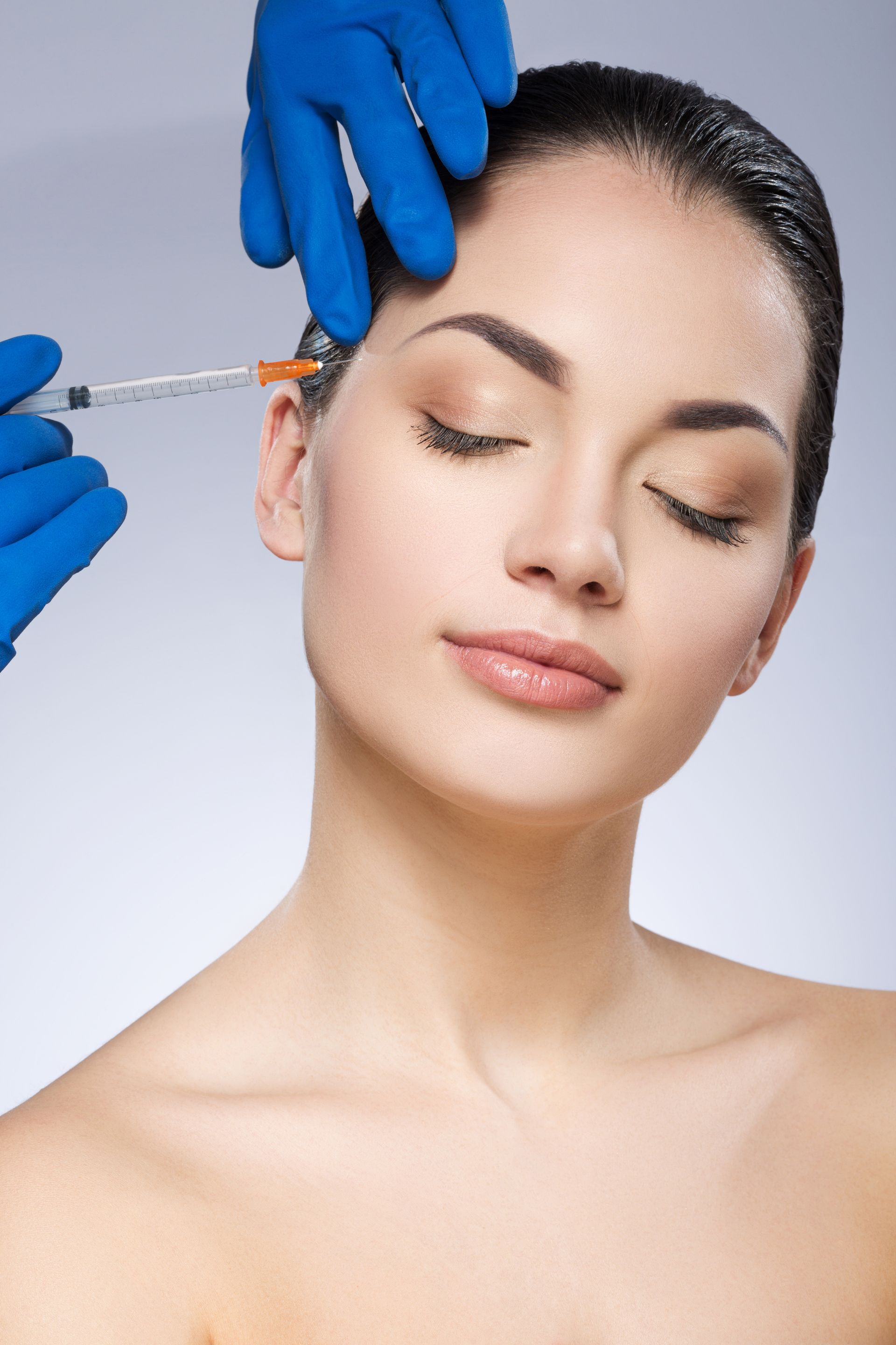 Person receiving a facial injection on a light blue background. Hands in blue gloves hold a syringe.