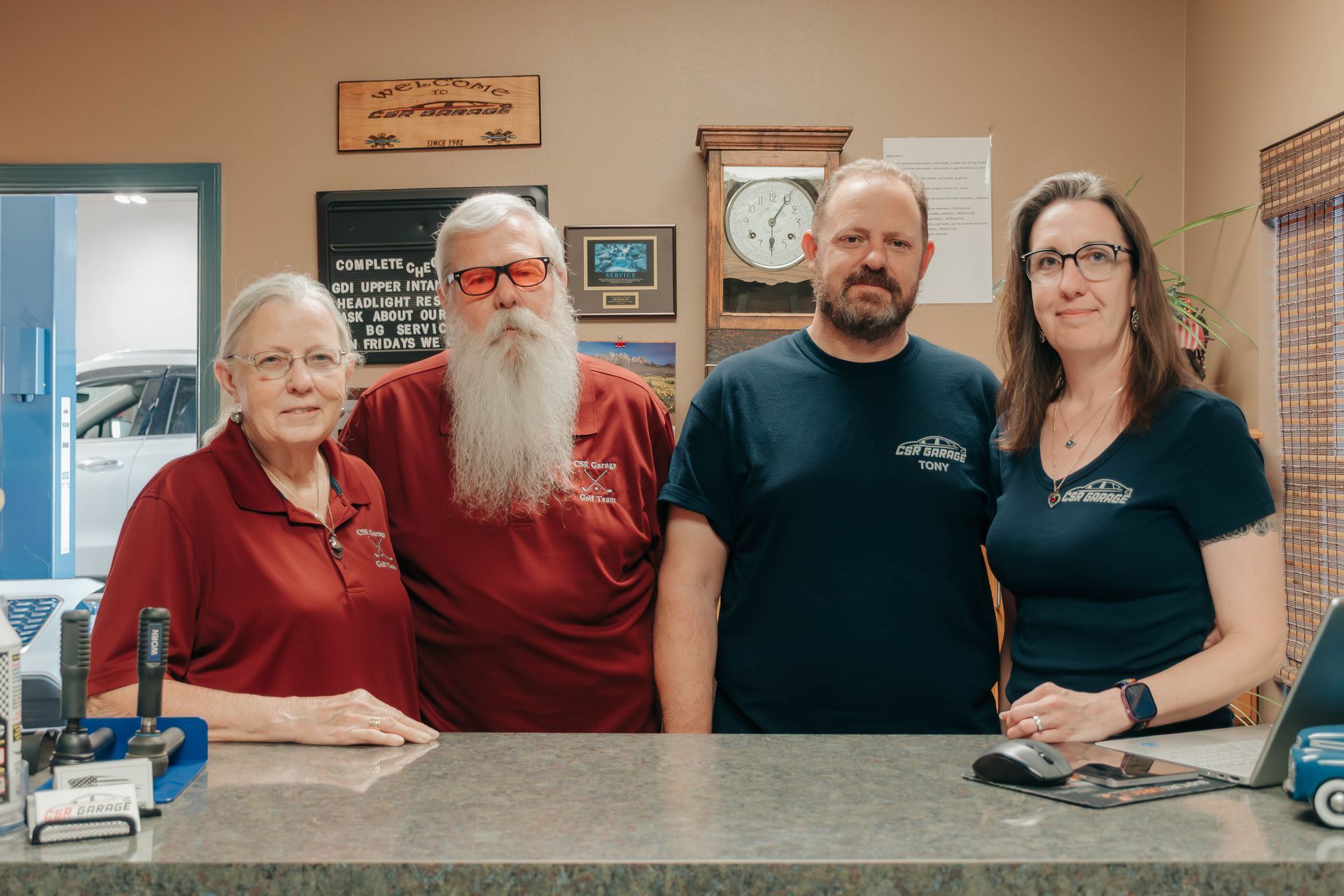 Four people standing behind a reception counter in an office, smiling at the camera.