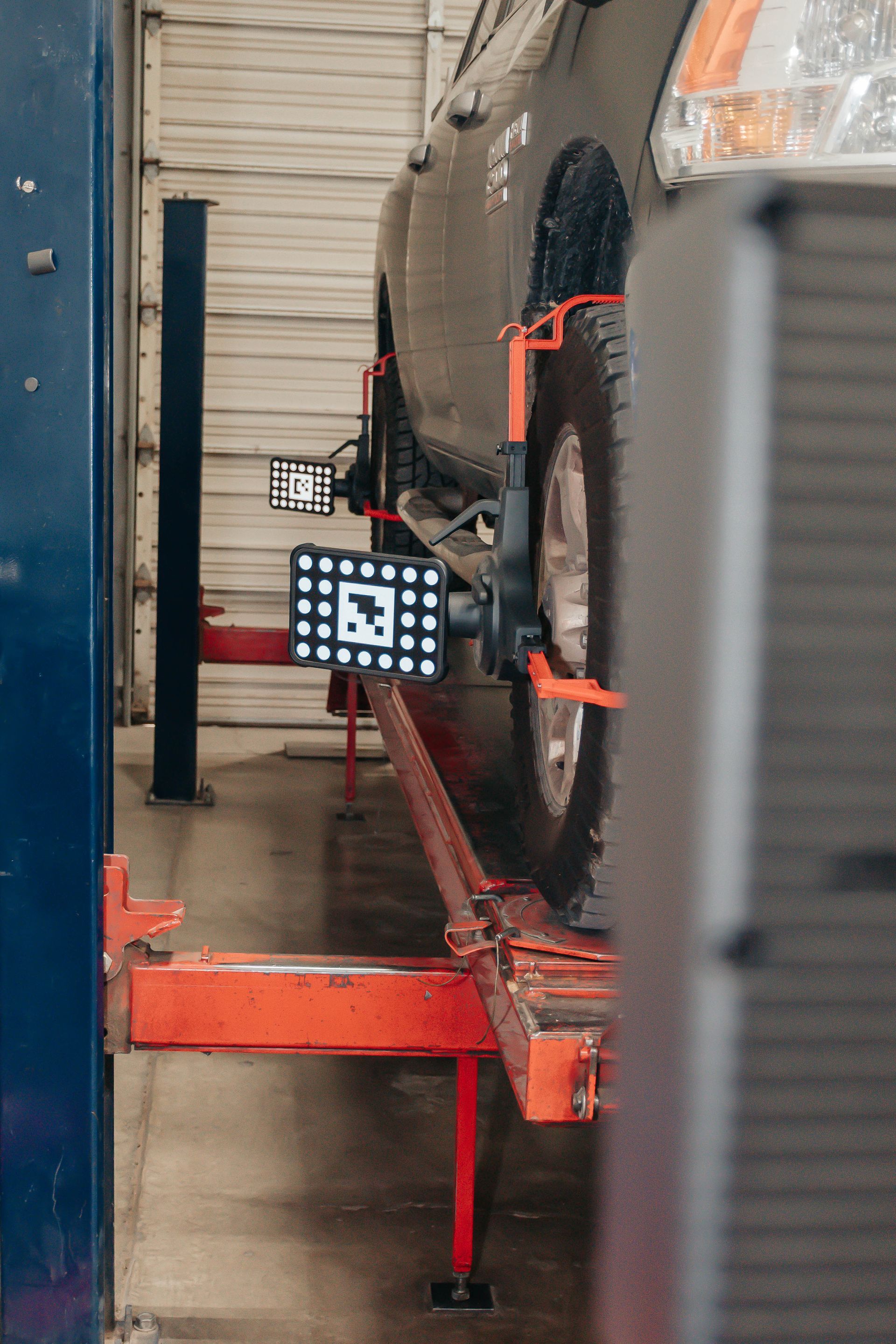 Van under repair on a lift, with red supports and a worker visible in the garage.