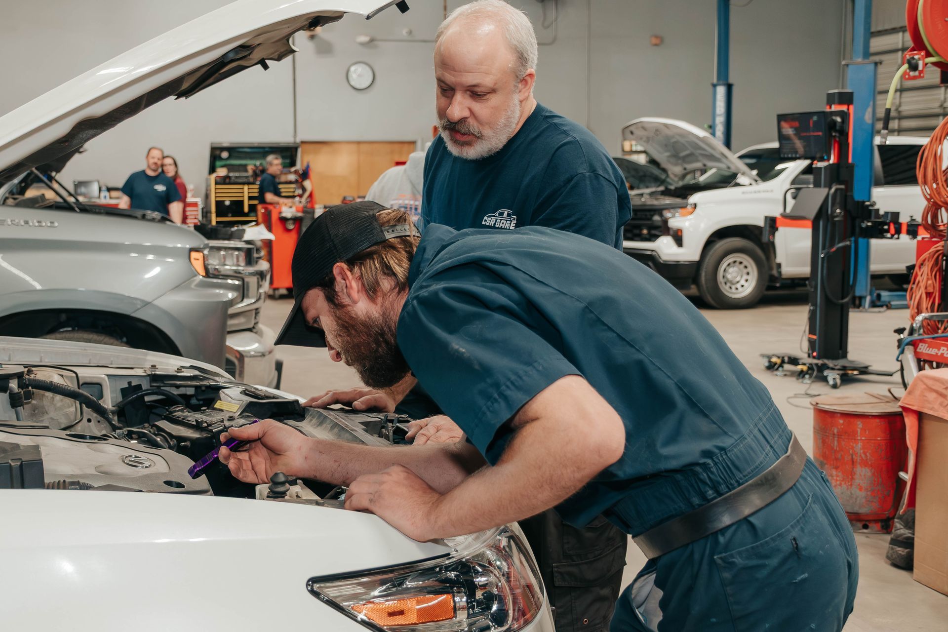 Mechanic working under open car hood in a busy auto repair shop