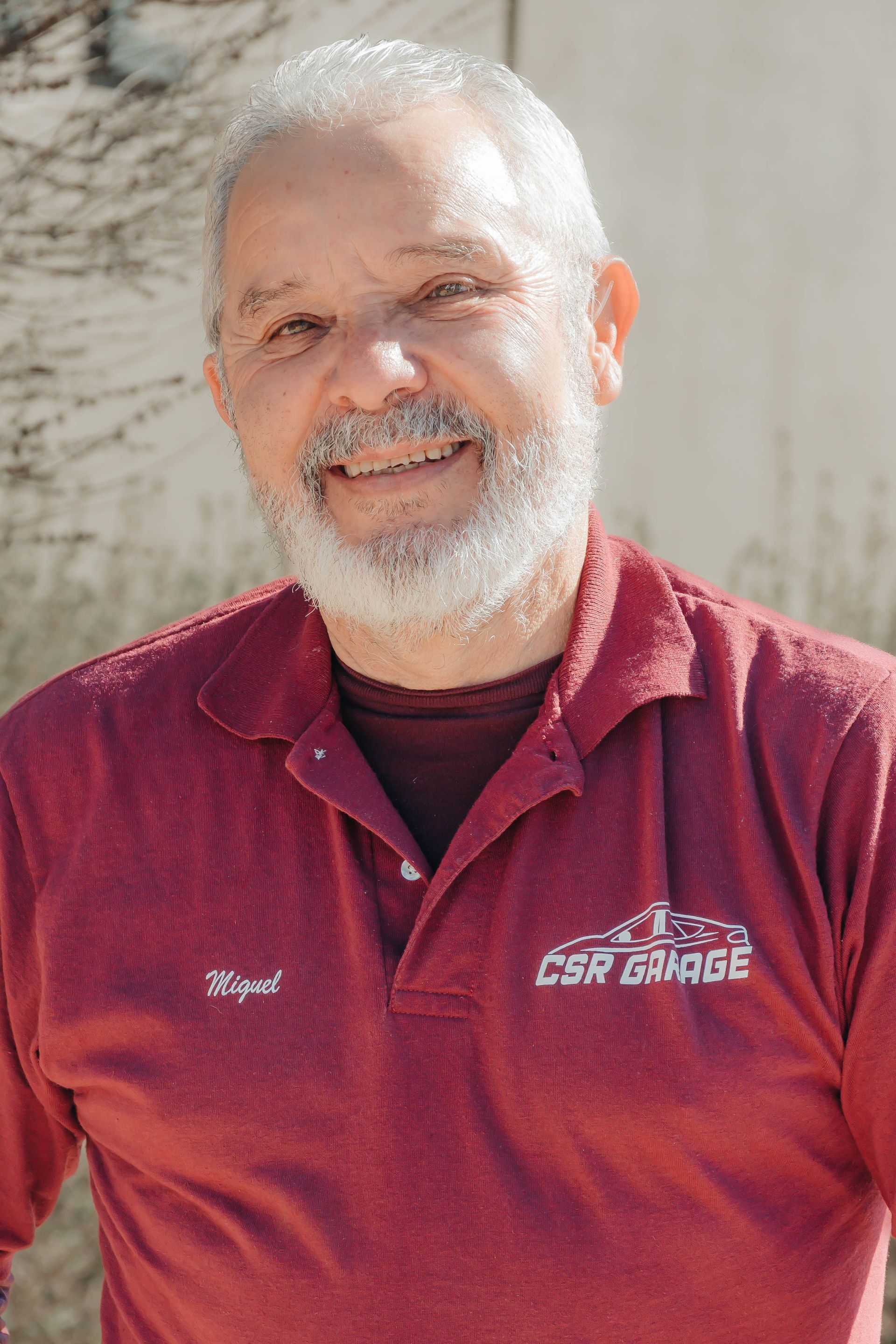 Smiling man in a red polo shirt standing outdoors against a light wall