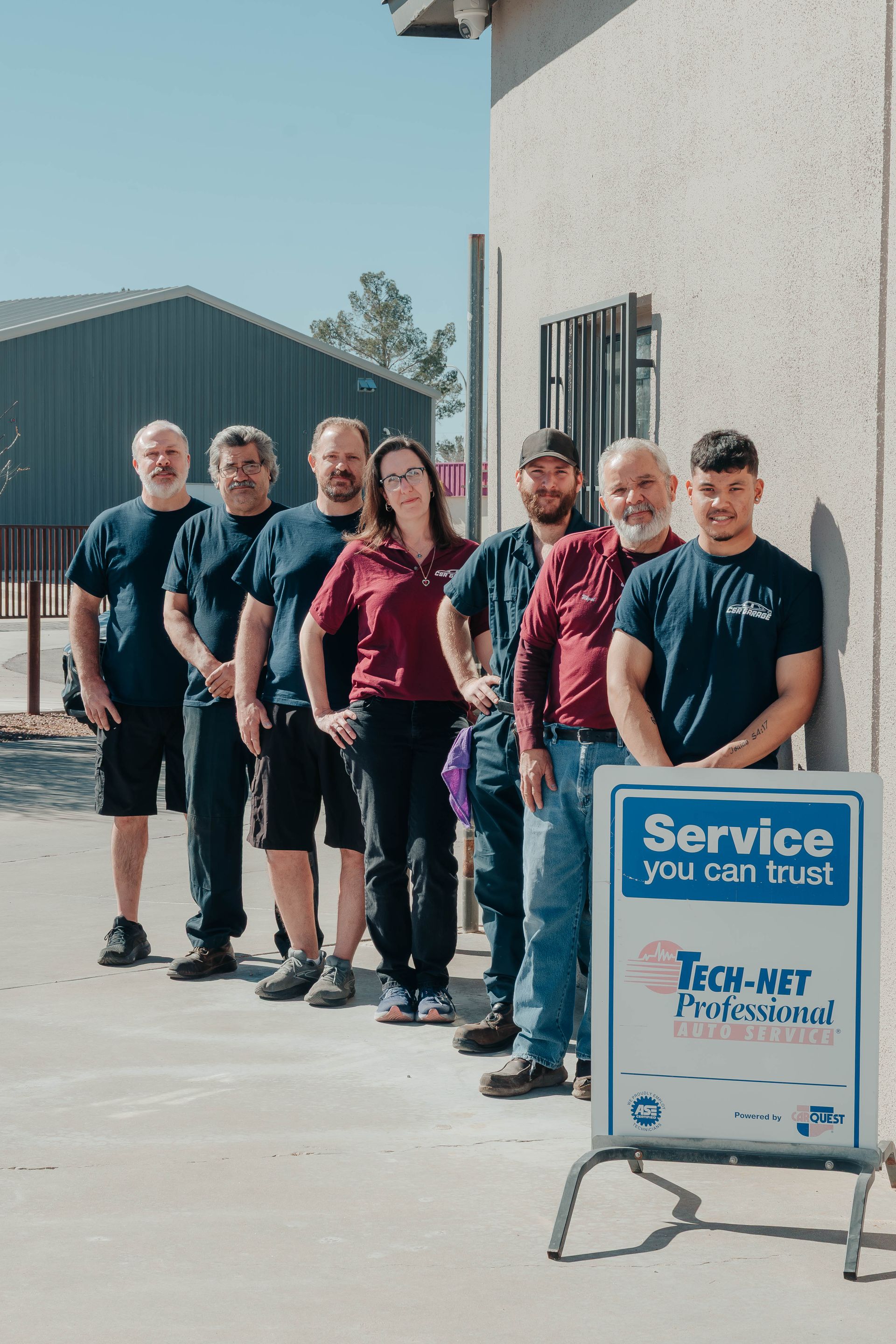 Seven people stand beside a building next to a blue sign reading “Services you can trust.”