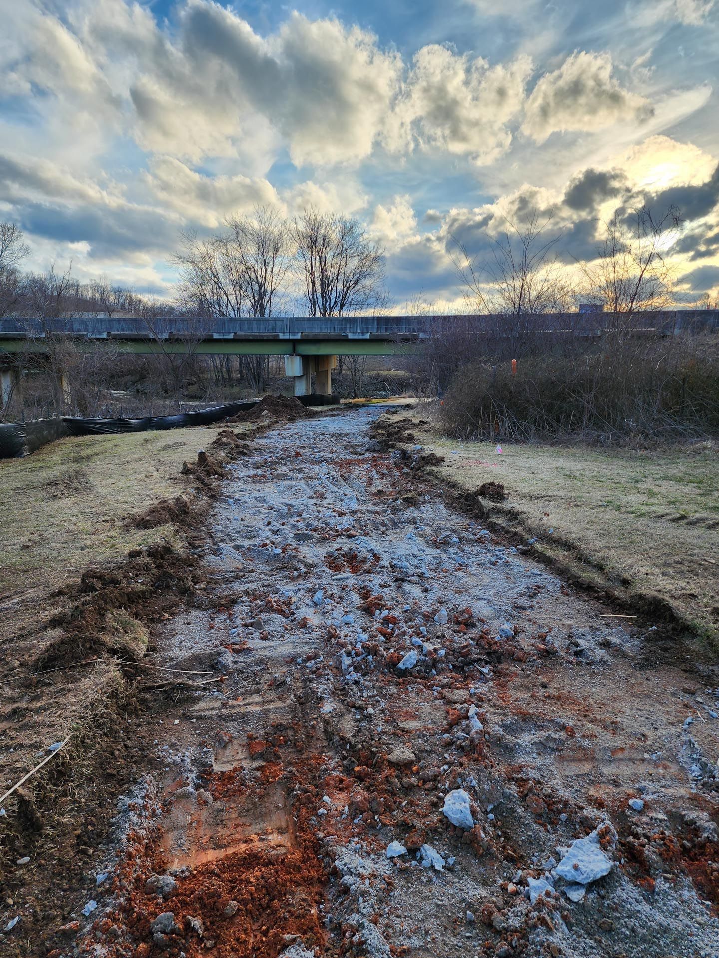 A muddy path leading to a bridge with a cloudy sky in the background.