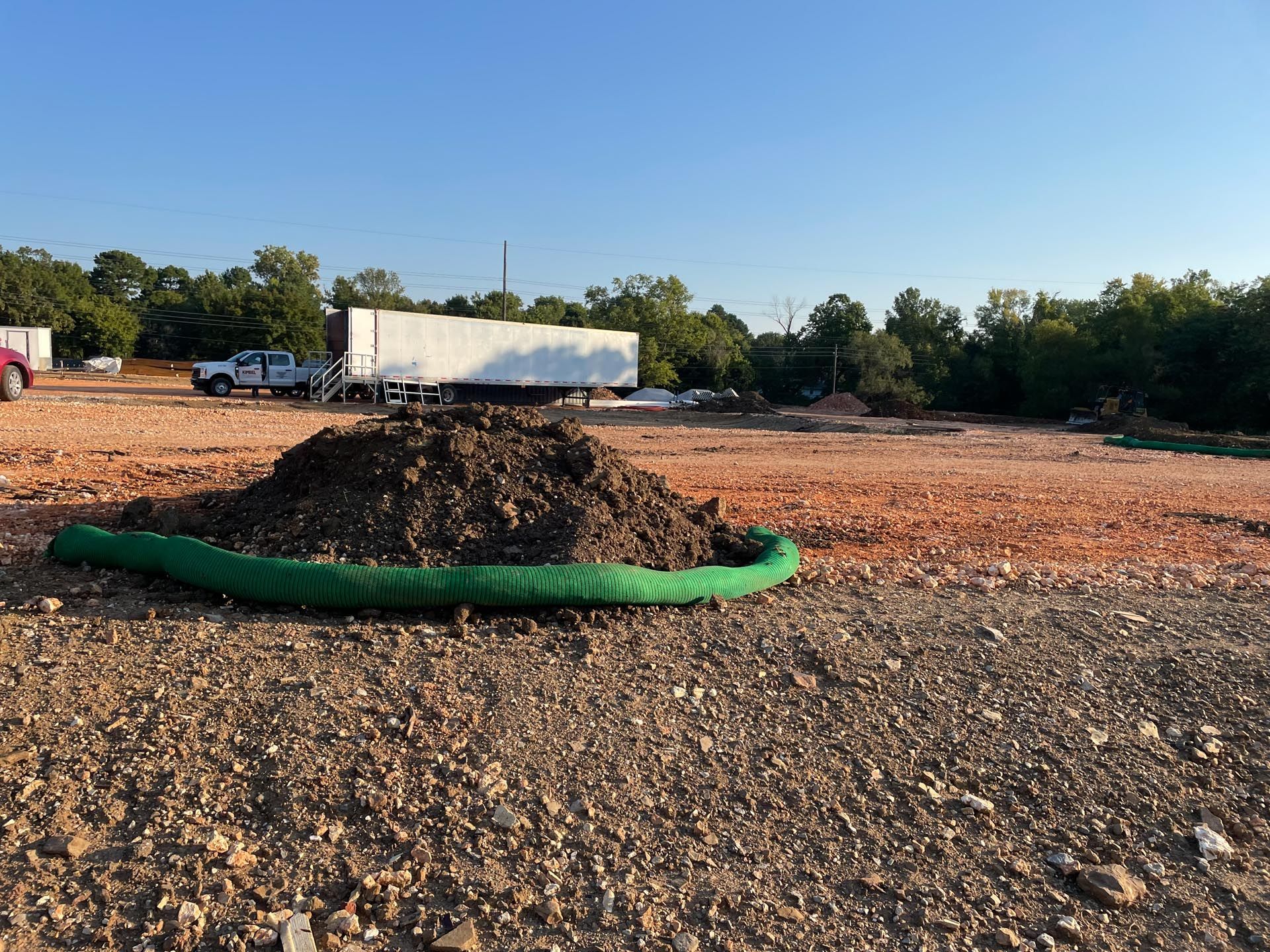 A pile of dirt and a green hose in a dirt field.