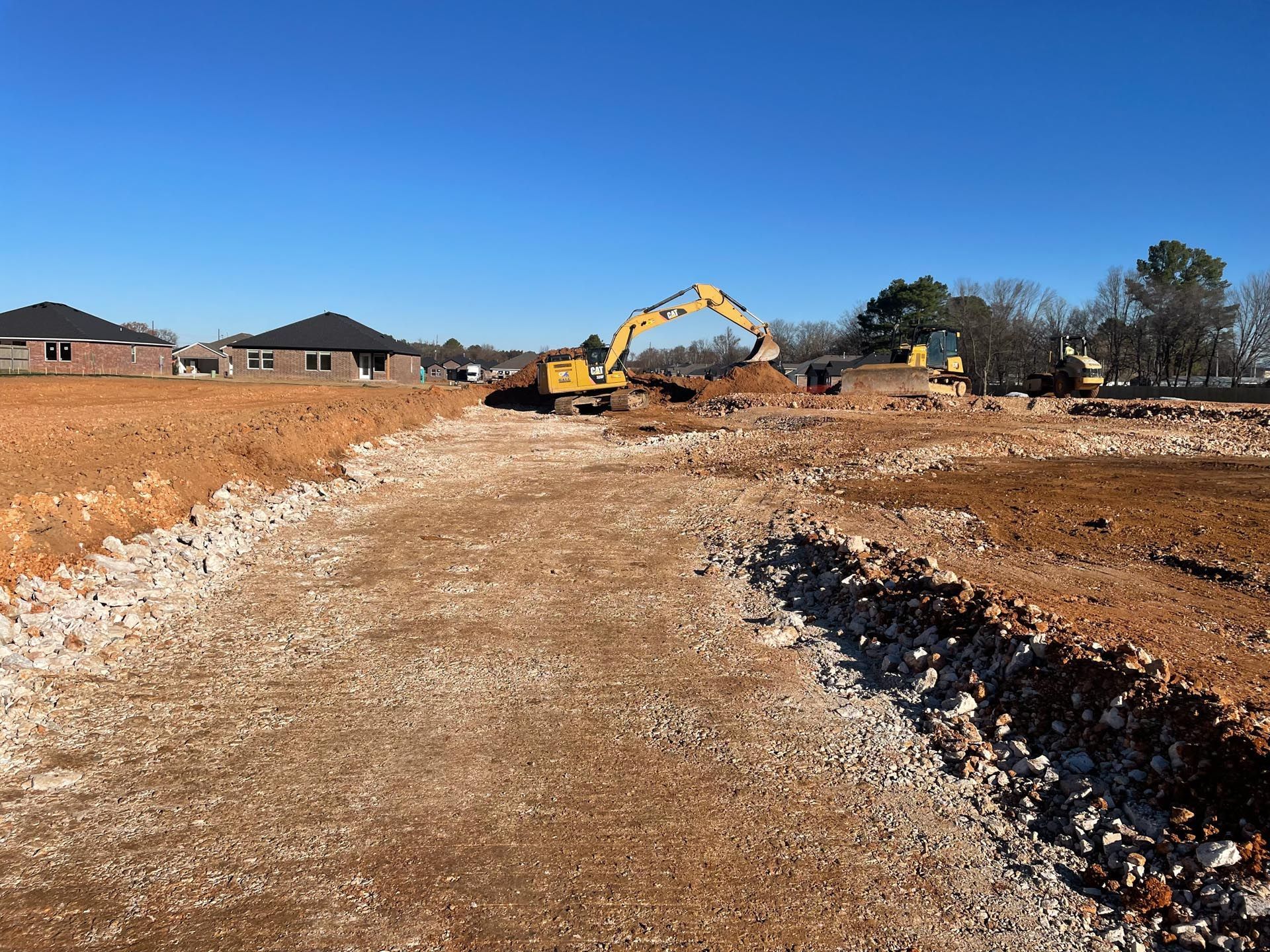A yellow excavator is working on a dirt road in a construction site.