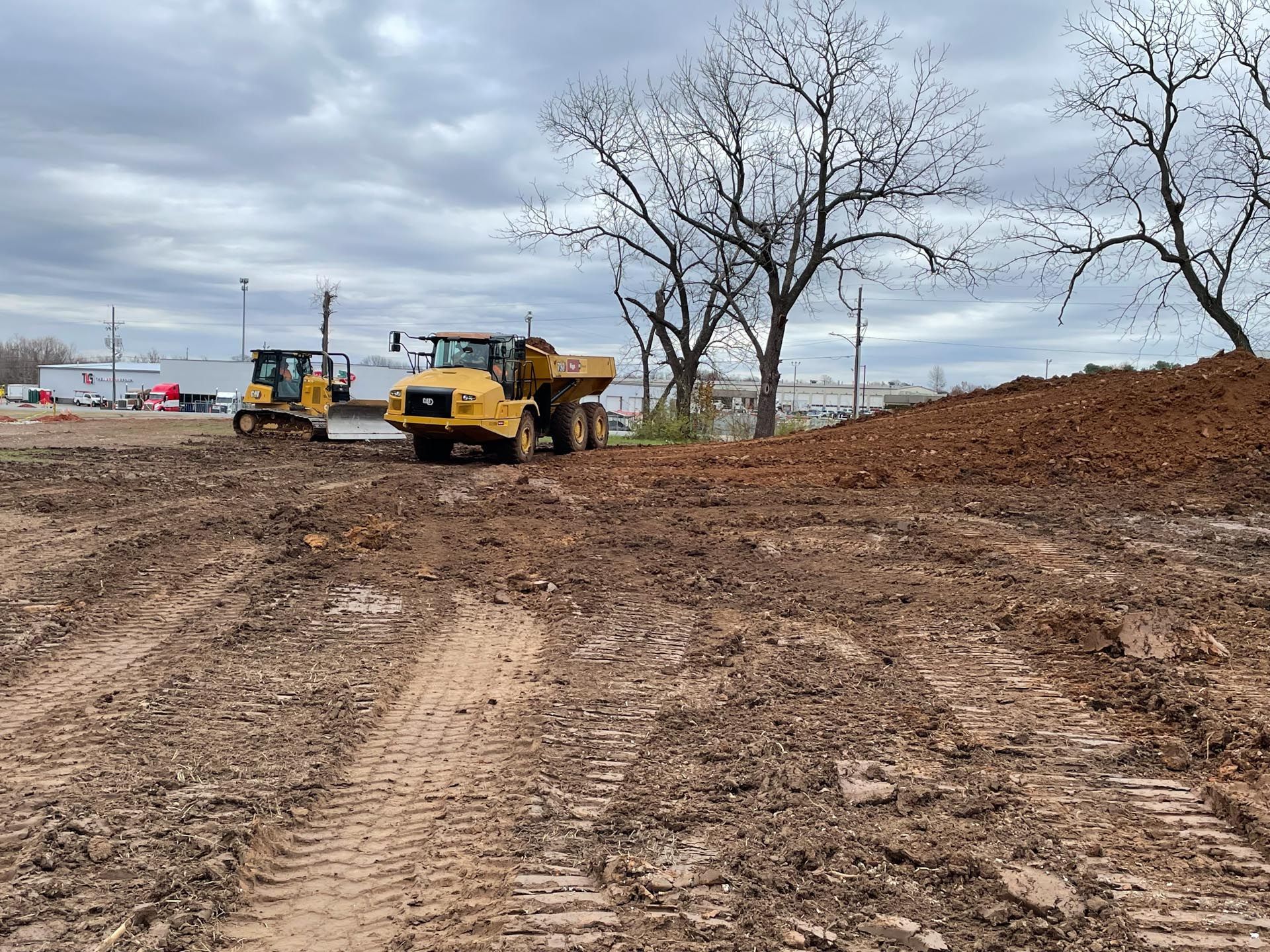 A dump truck is driving down a dirt road next to a bulldozer.
