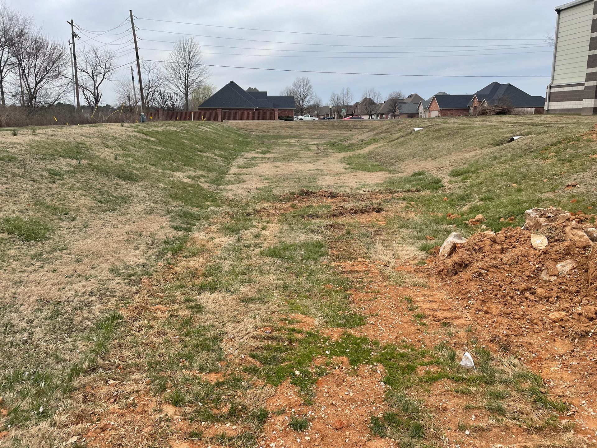 A dirt road going through a grassy field with houses in the background.