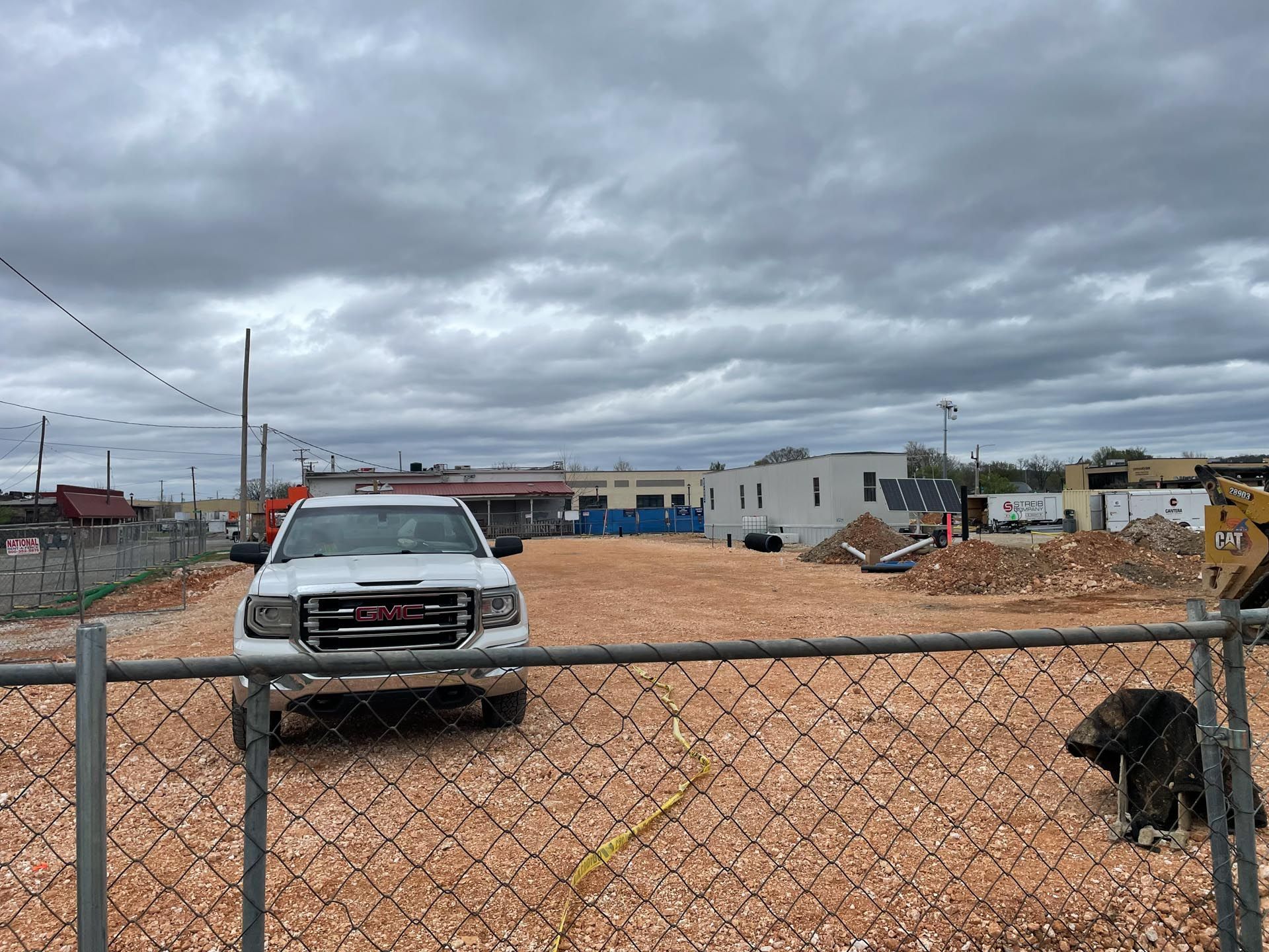 A white truck is parked in a dirt lot behind a chain link fence.