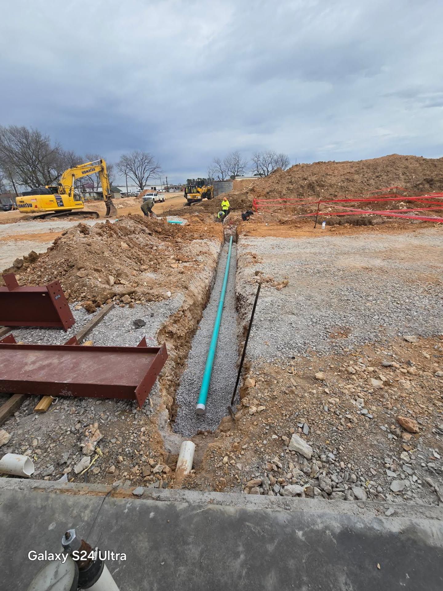A construction site with a lot of dirt and a yellow excavator in the background.