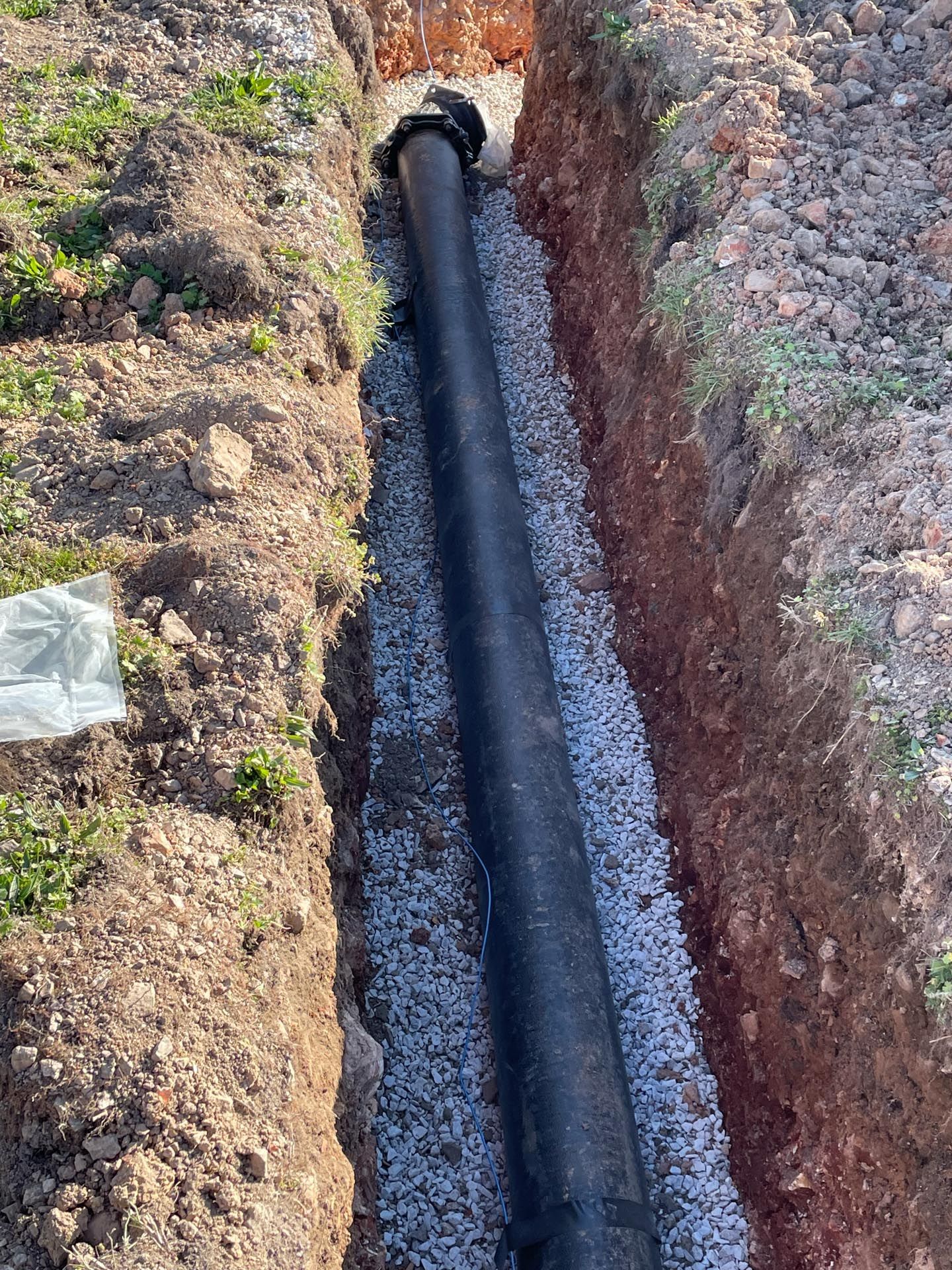 A large black pipe is being installed in a trench.