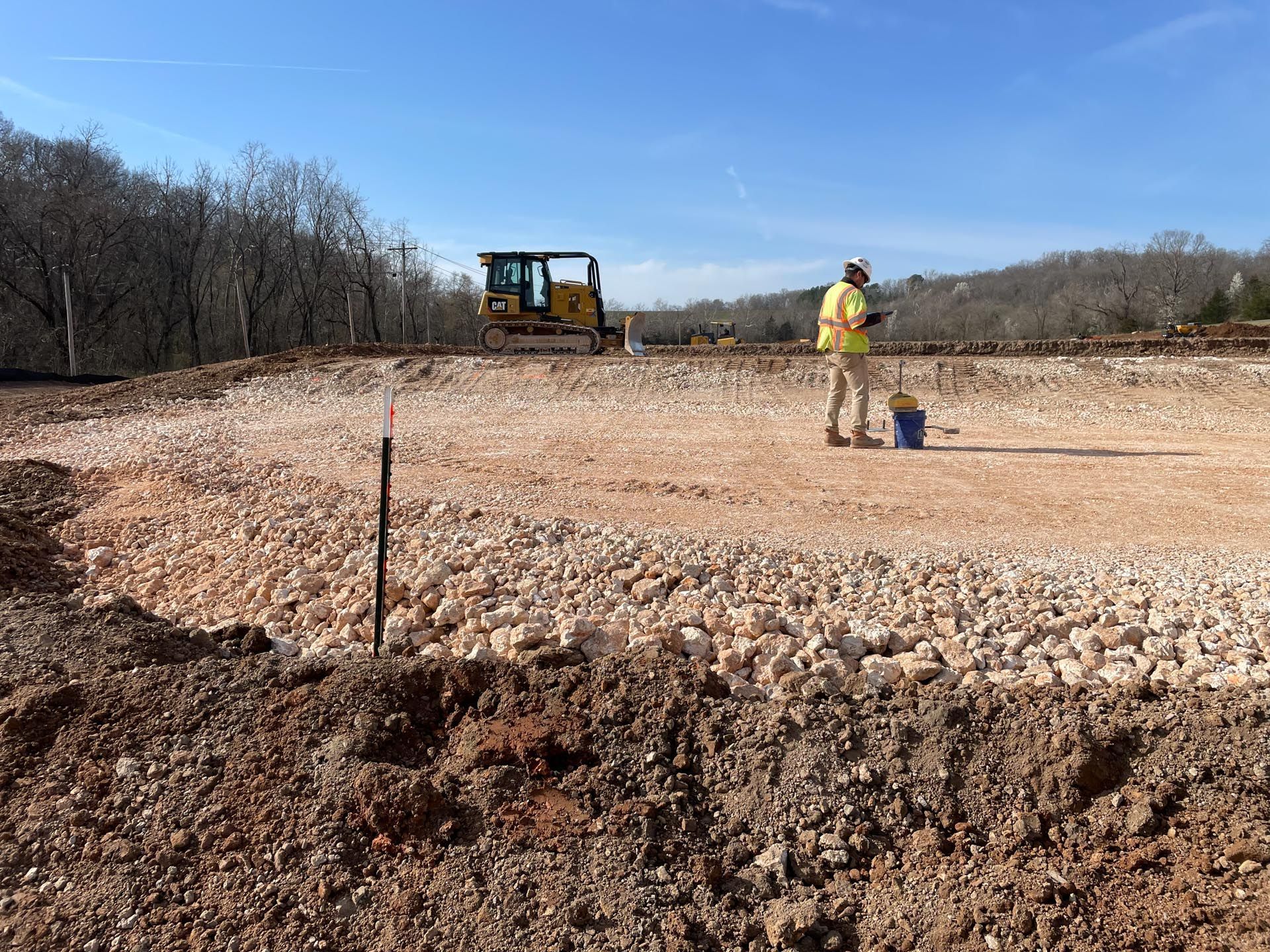 A man is standing in a dirt field with a bulldozer in the background.