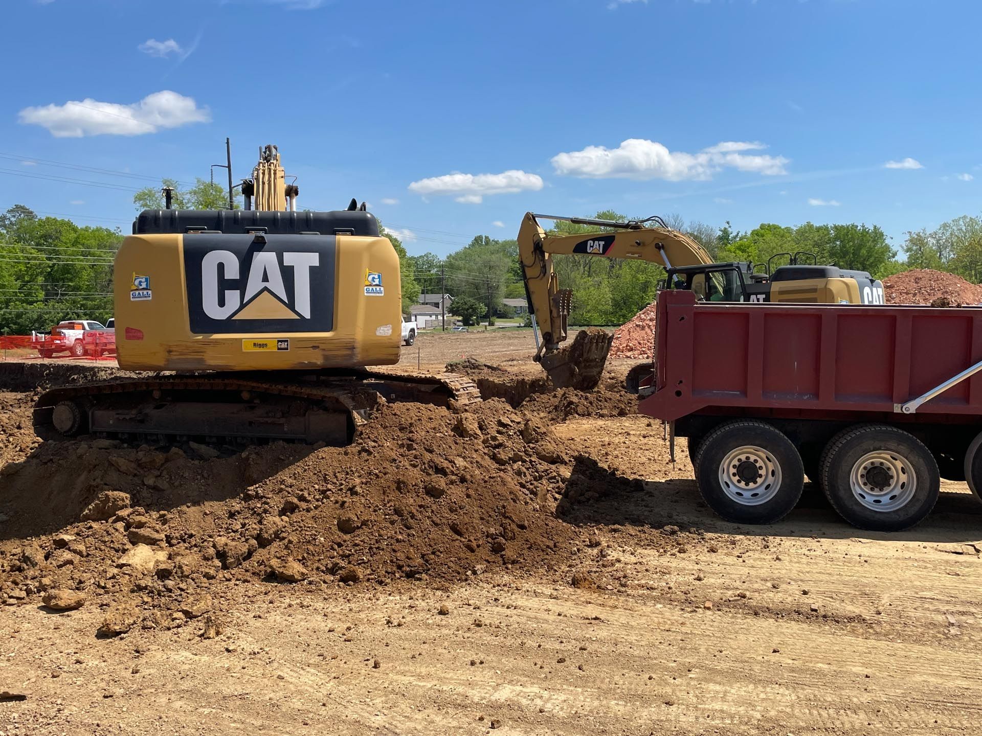 A cat excavator is digging a hole next to a dump truck.