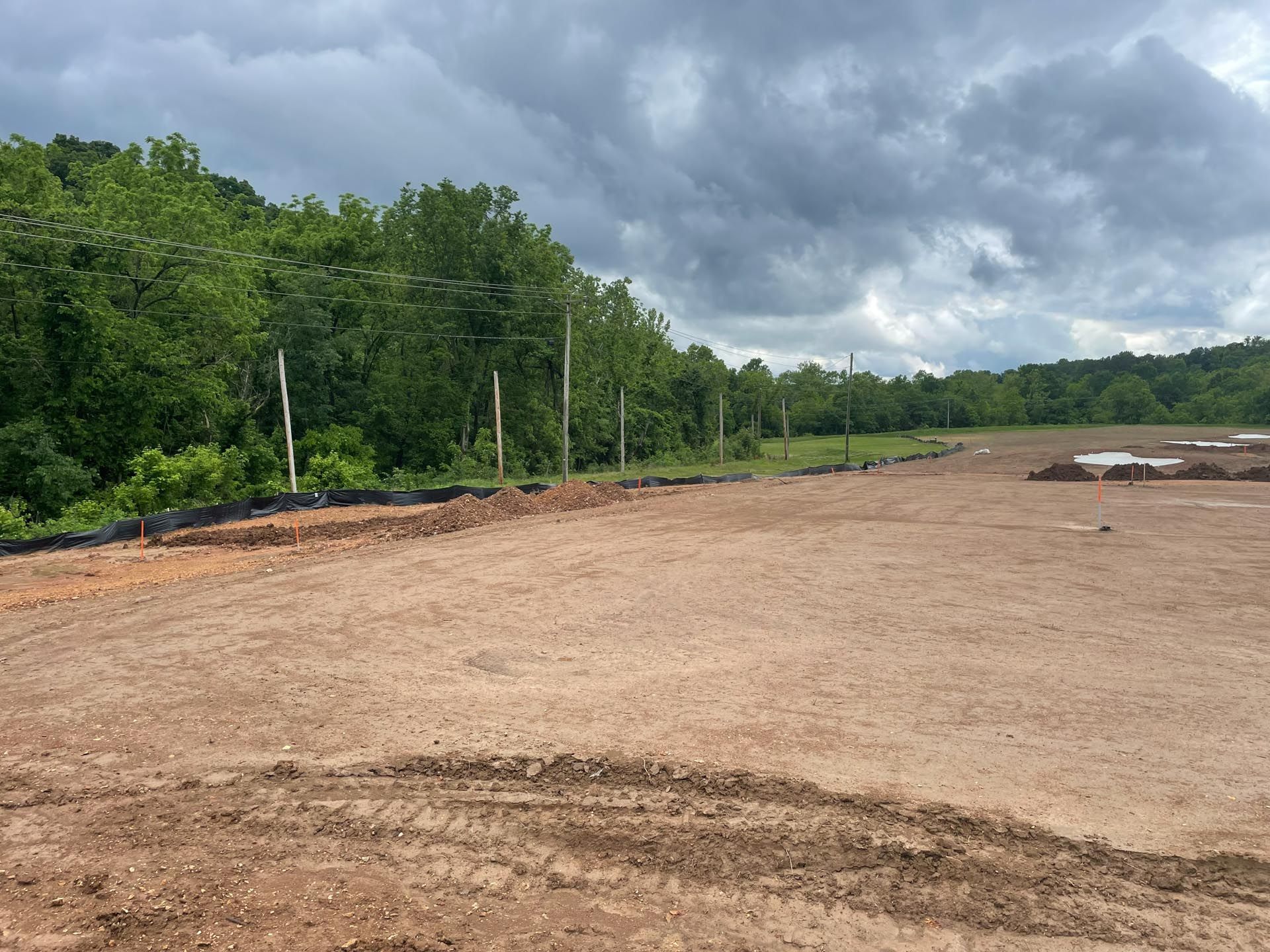 A dirt field with trees in the background and a cloudy sky