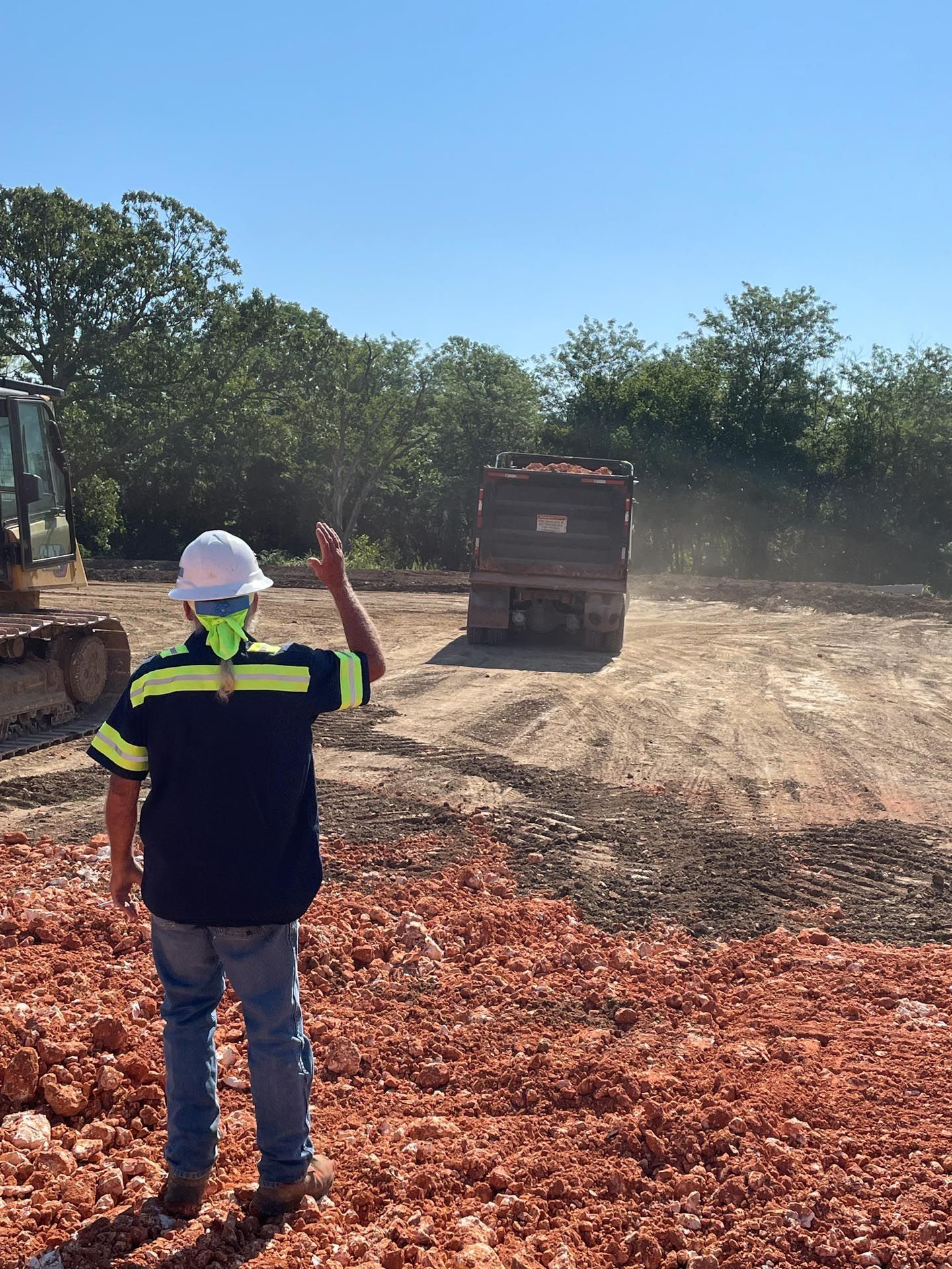 A man in a hard hat is standing in front of a dump truck.