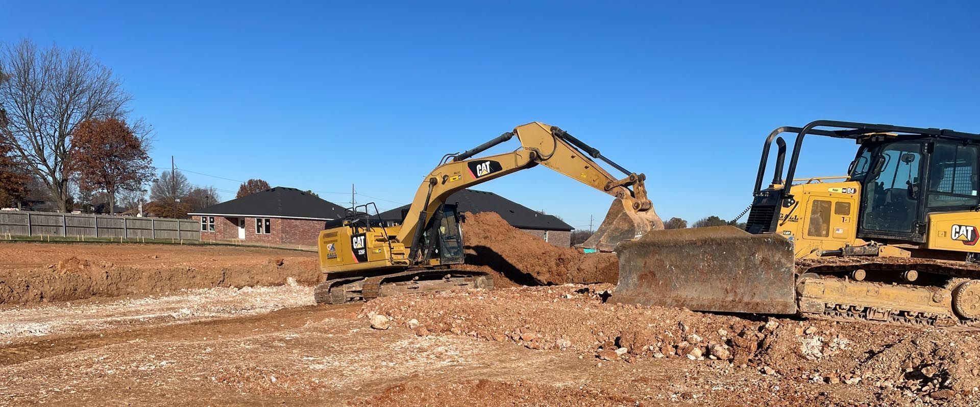 Two construction vehicles are working in a dirt field.