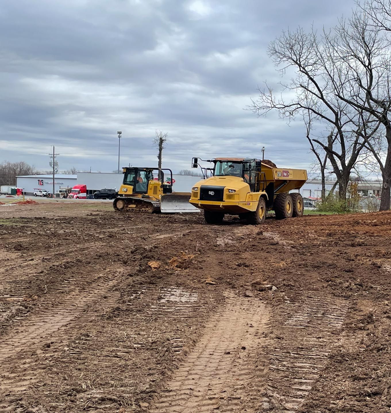 A dump truck and a bulldozer are parked in a dirt field.