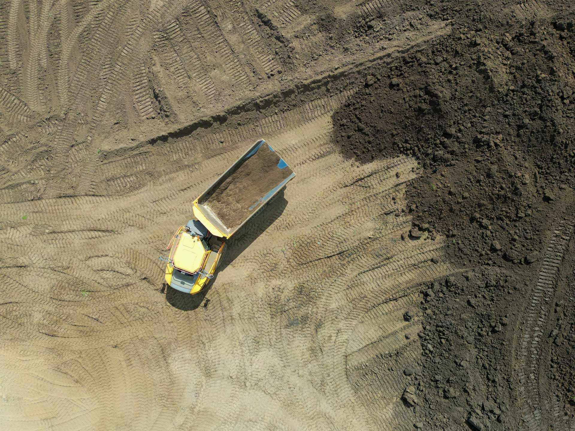 An aerial view of a dump truck driving through a dirt field.