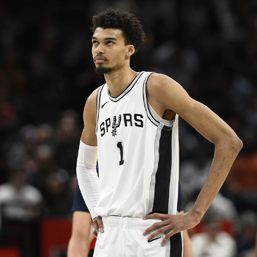A basketball player for the spurs is standing on the court with his hands on his hips.