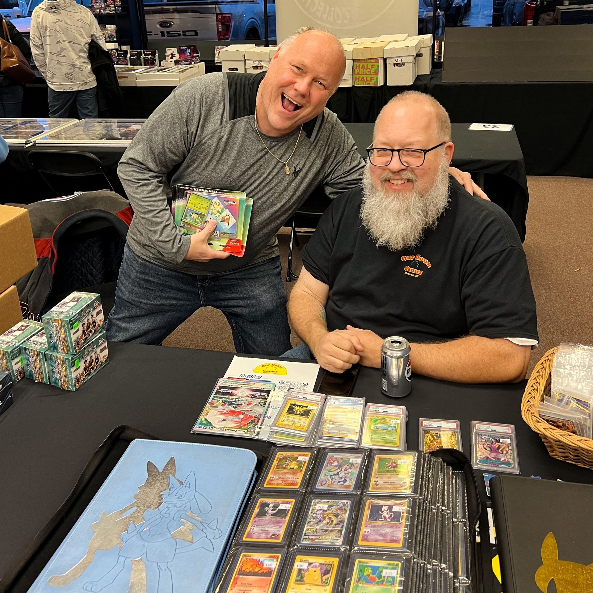 Two men are posing for a picture at a table full of cards