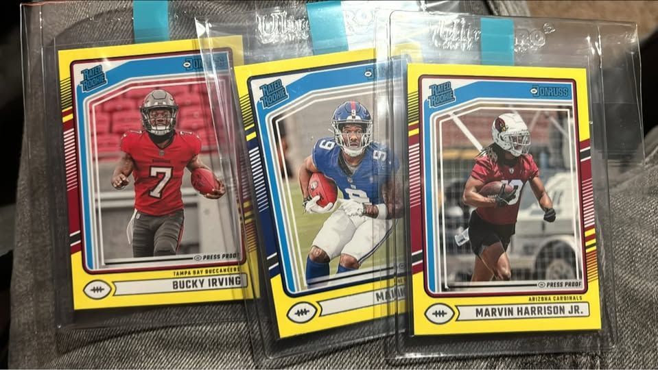 Three football cards are sitting on top of each other on a table.