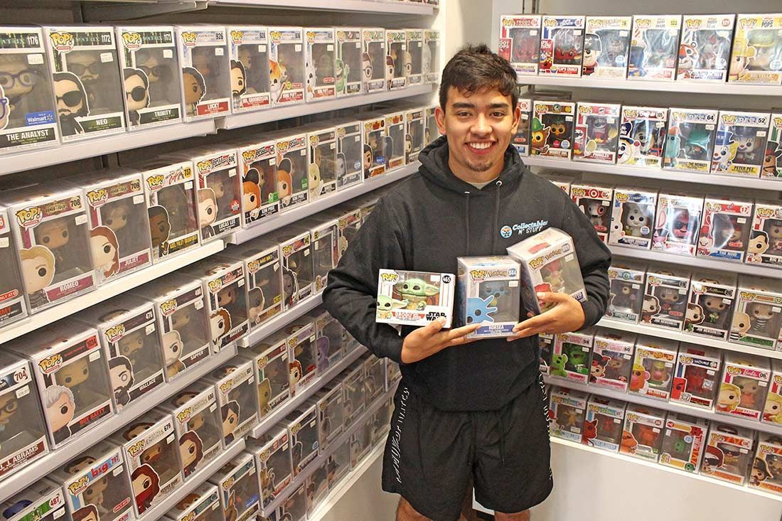 Person holding Funko Pop figures in a store with shelves filled with collectible figures.
