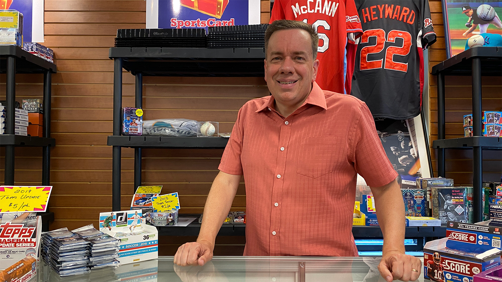 Man smiling in a sports memorabilia store, leaning on a counter with baseball cards.