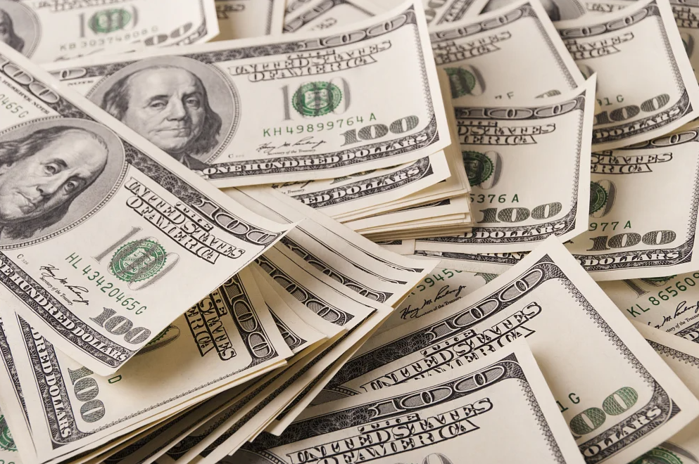 Pile of US $100 bills, featuring Benjamin Franklin's portrait, on a white surface.