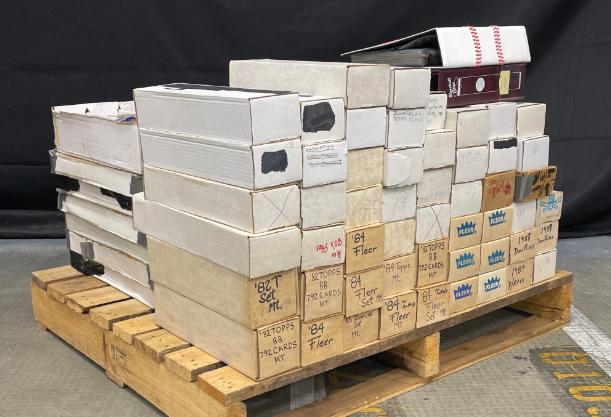 A pallet stacked with many cardboard boxes of various sizes, likely holding trading cards. Get More 