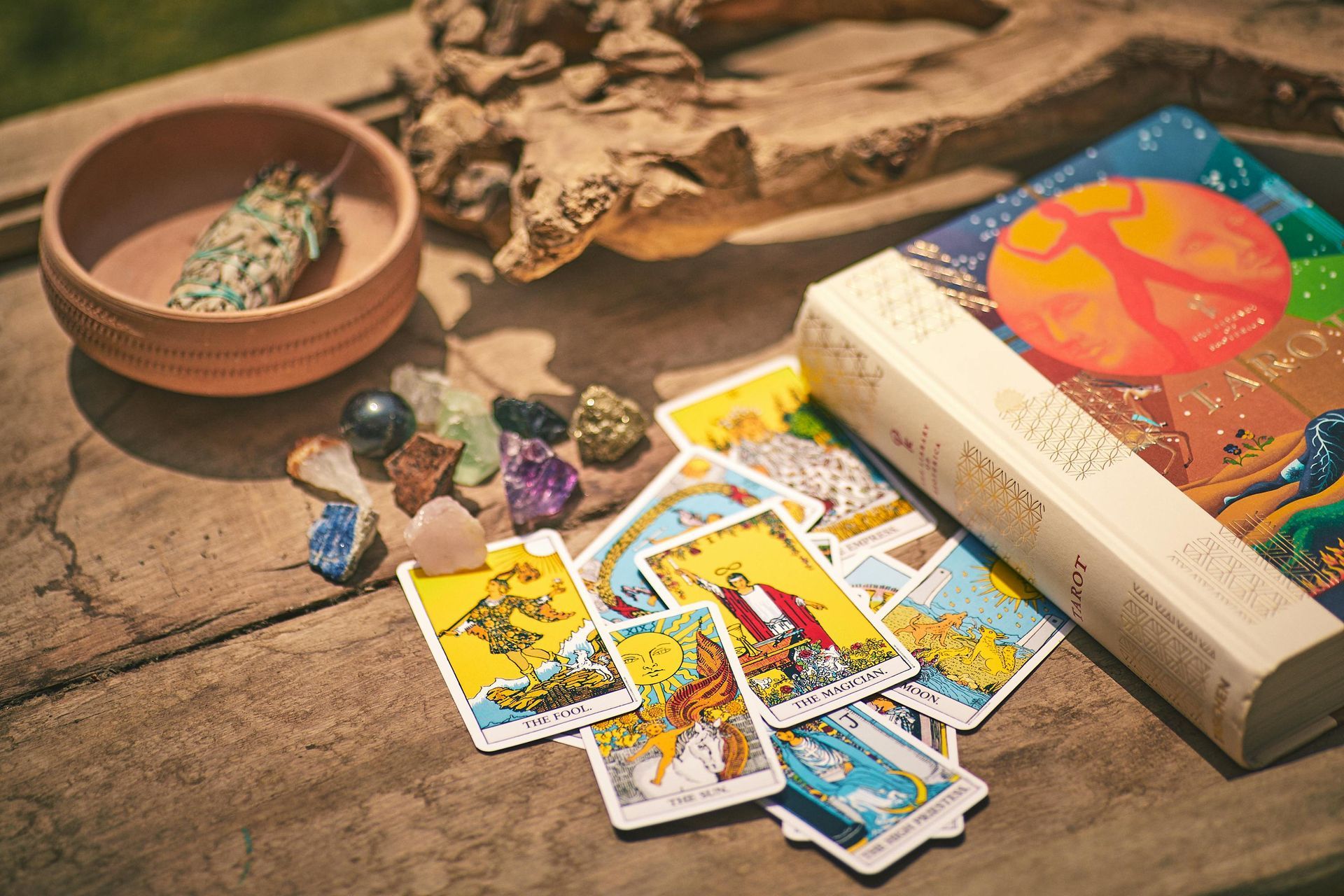 Tarot cards, crystals, incense, and sage bowl on a wooden surface, suggesting divination practice.