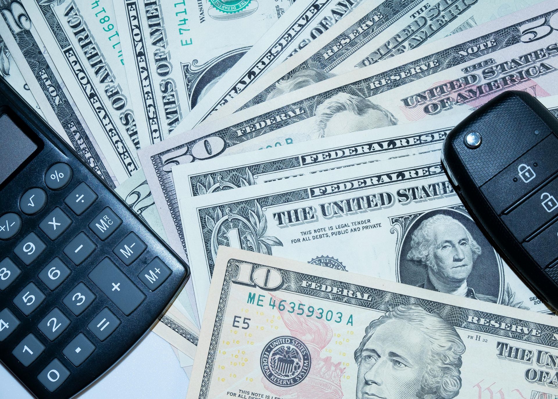 Calculator and car key on a fan of US dollar bills.