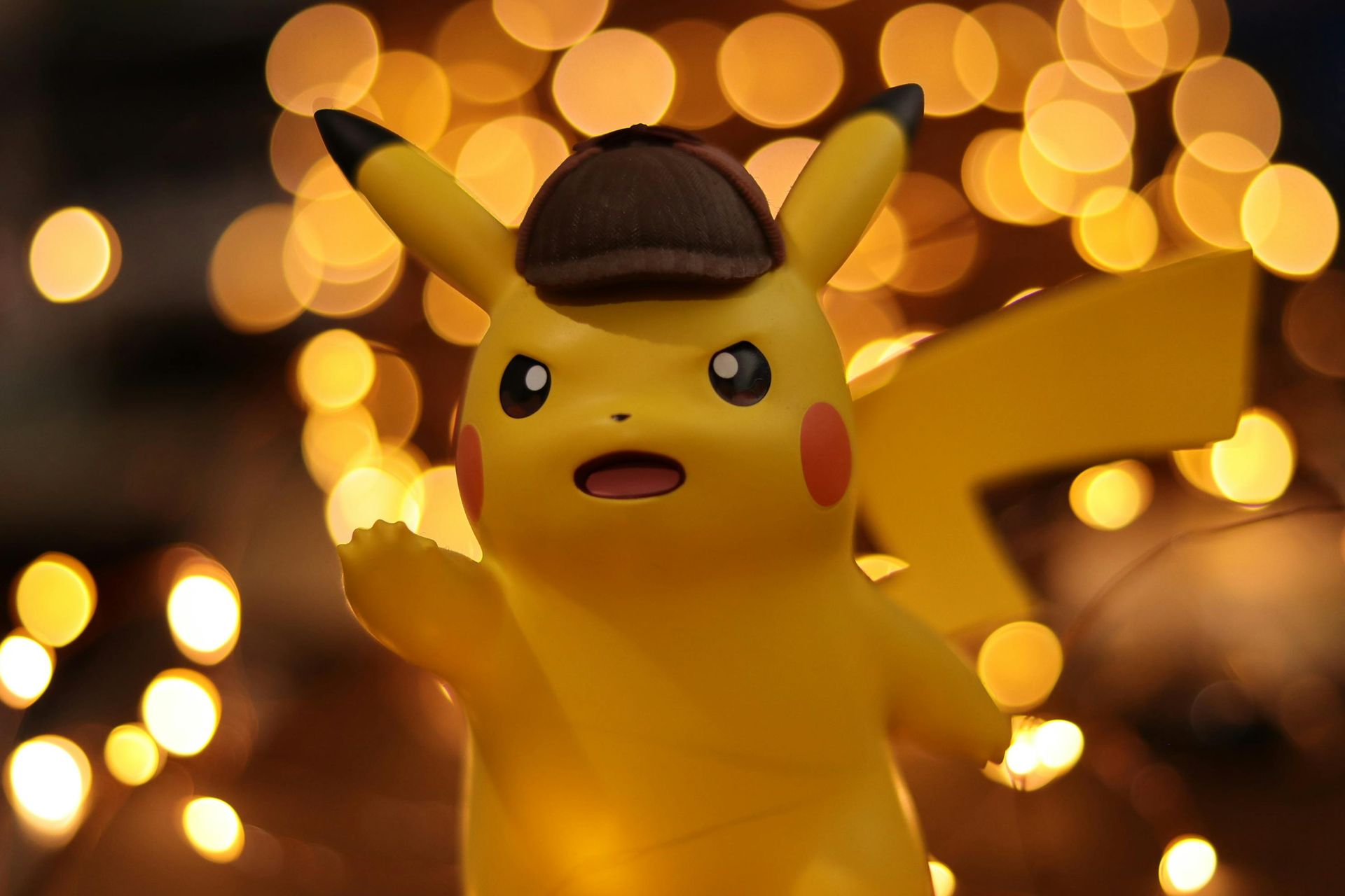 Pikachu wearing a detective hat, illuminated against a blurred background of warm, golden lights.
