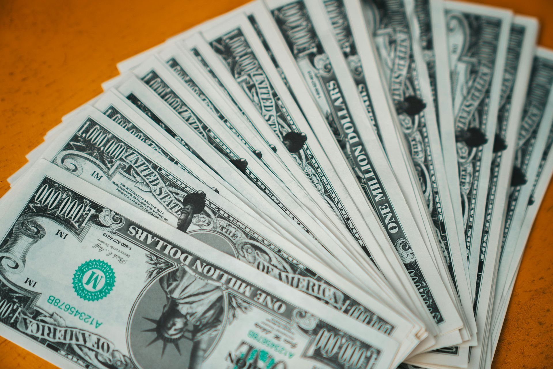 Fan of US one-dollar bills on a yellow surface.