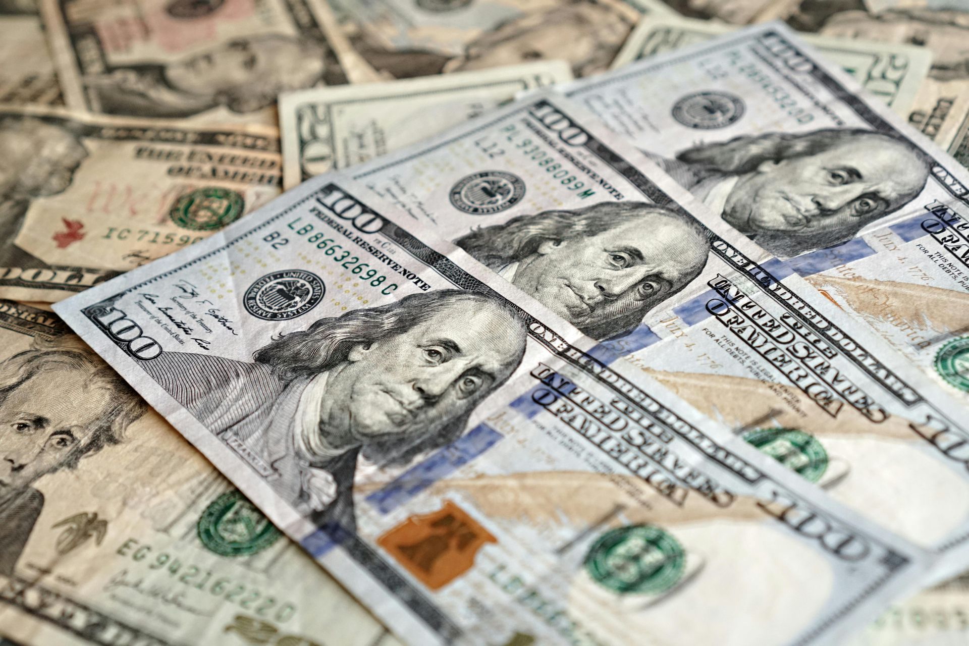 A stack of United States one-hundred-dollar bills with other denominations partially visible underneath.
