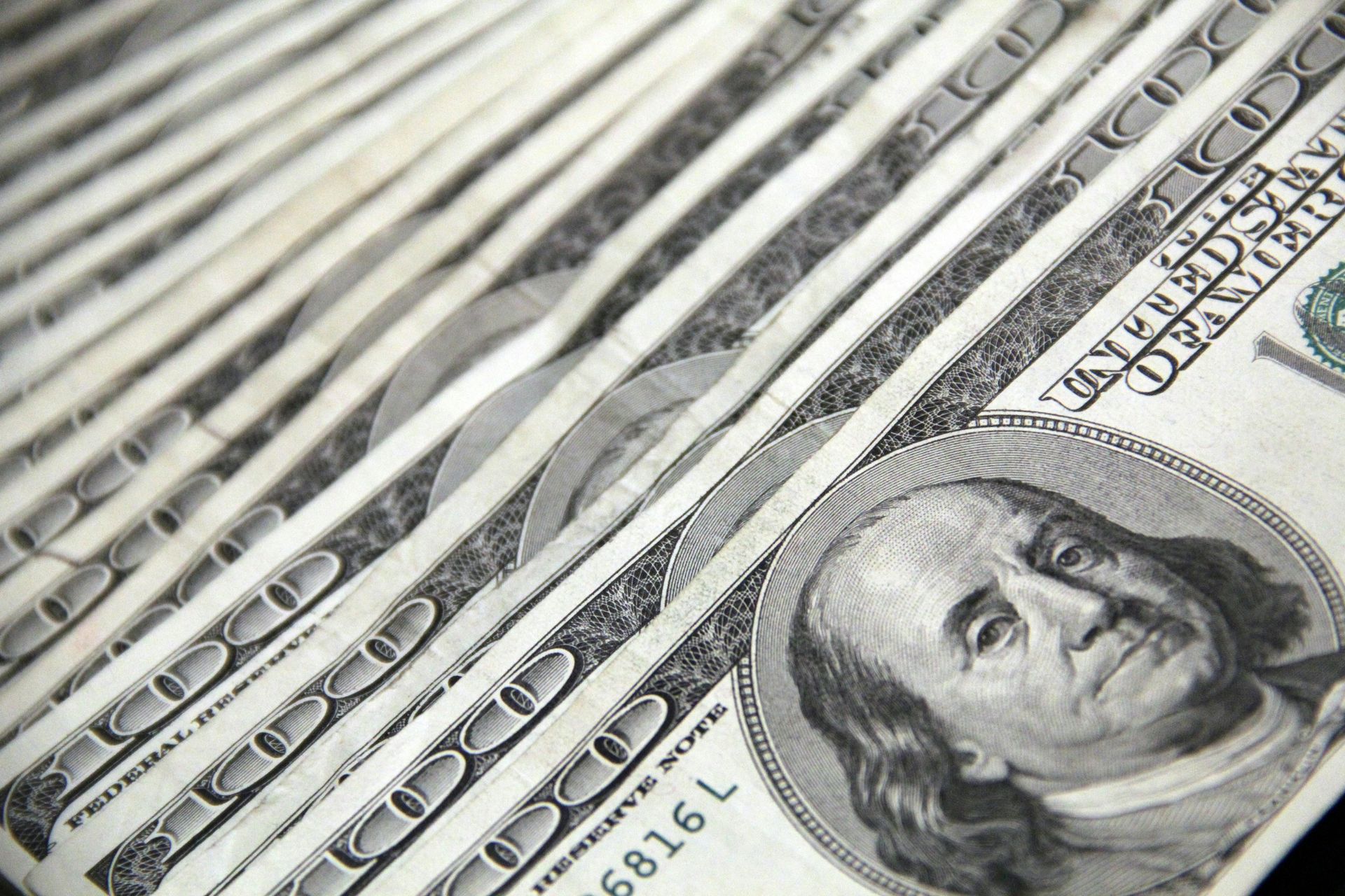 A fan of layered US one-hundred-dollar bills featuring Benjamin Franklin's portrait.