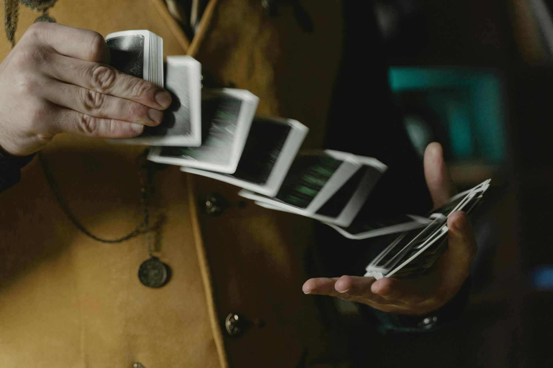 A person in a yellow vest performs a card spring flourish, cascading a deck of cards between their hands.