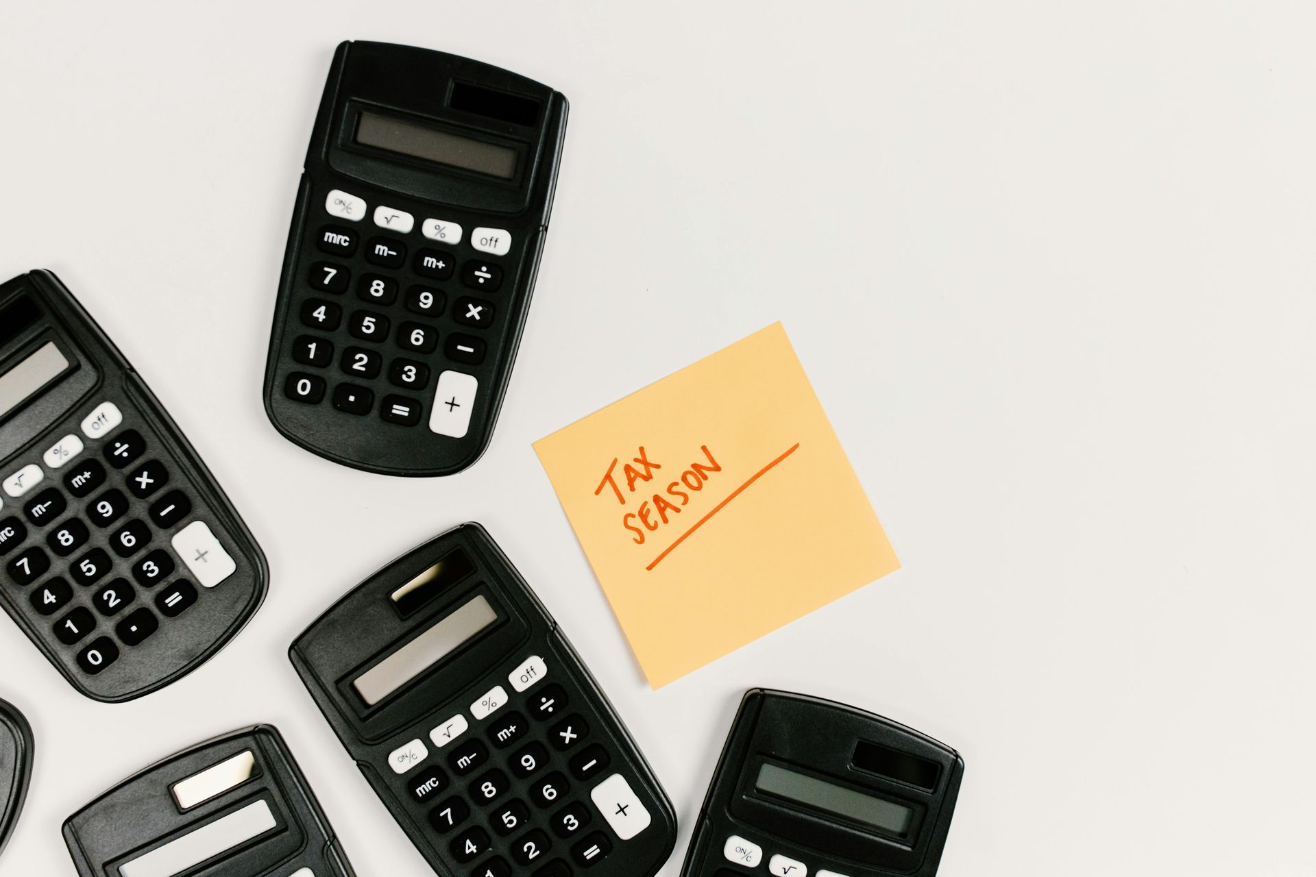 Several black calculators arranged on a white surface, with a yellow sticky note reading 