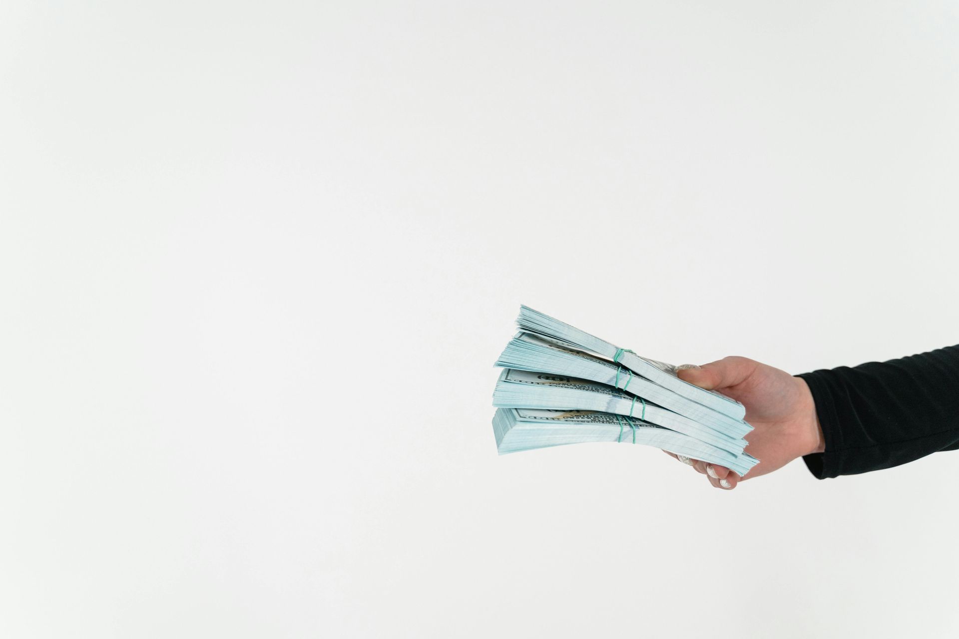 A hand extends a stack of teal-colored banknotes against a plain white background.