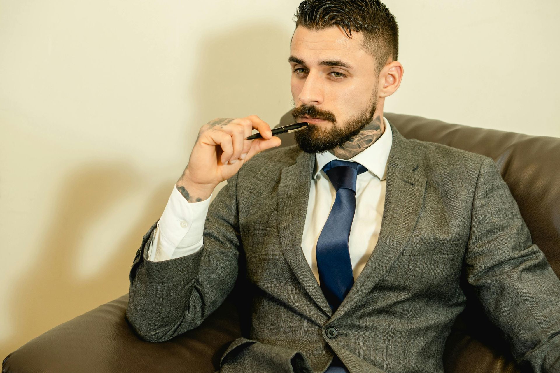 Man in suit holding a vape pen, sitting in a leather chair.