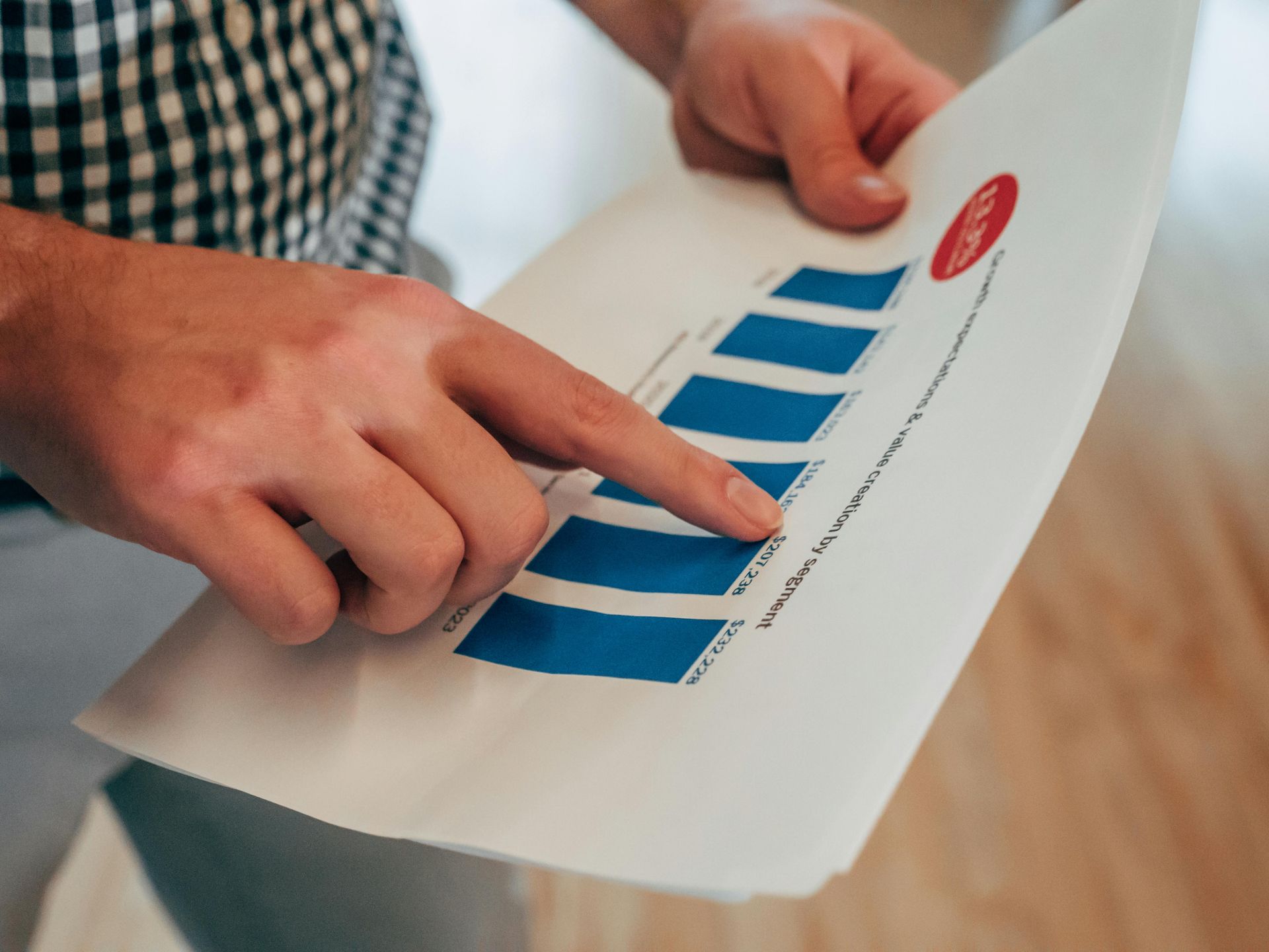 A person points to a blue bar graph on a document held in their hands.